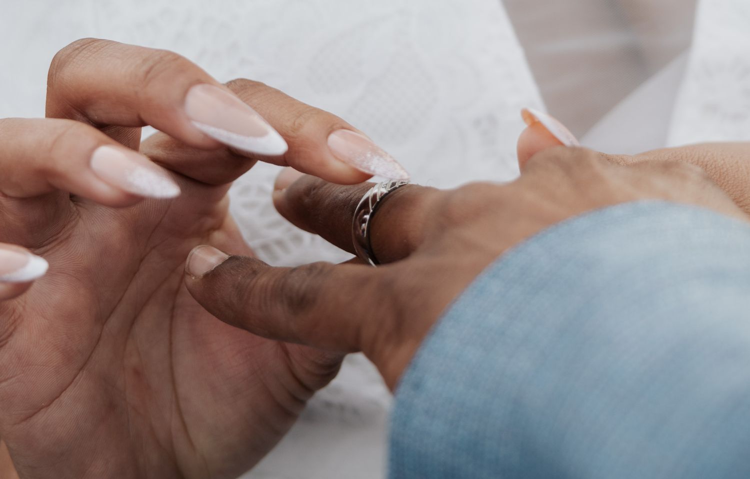 Close-up of diamond wedding ring being placed on bride's hand with manicured nails.