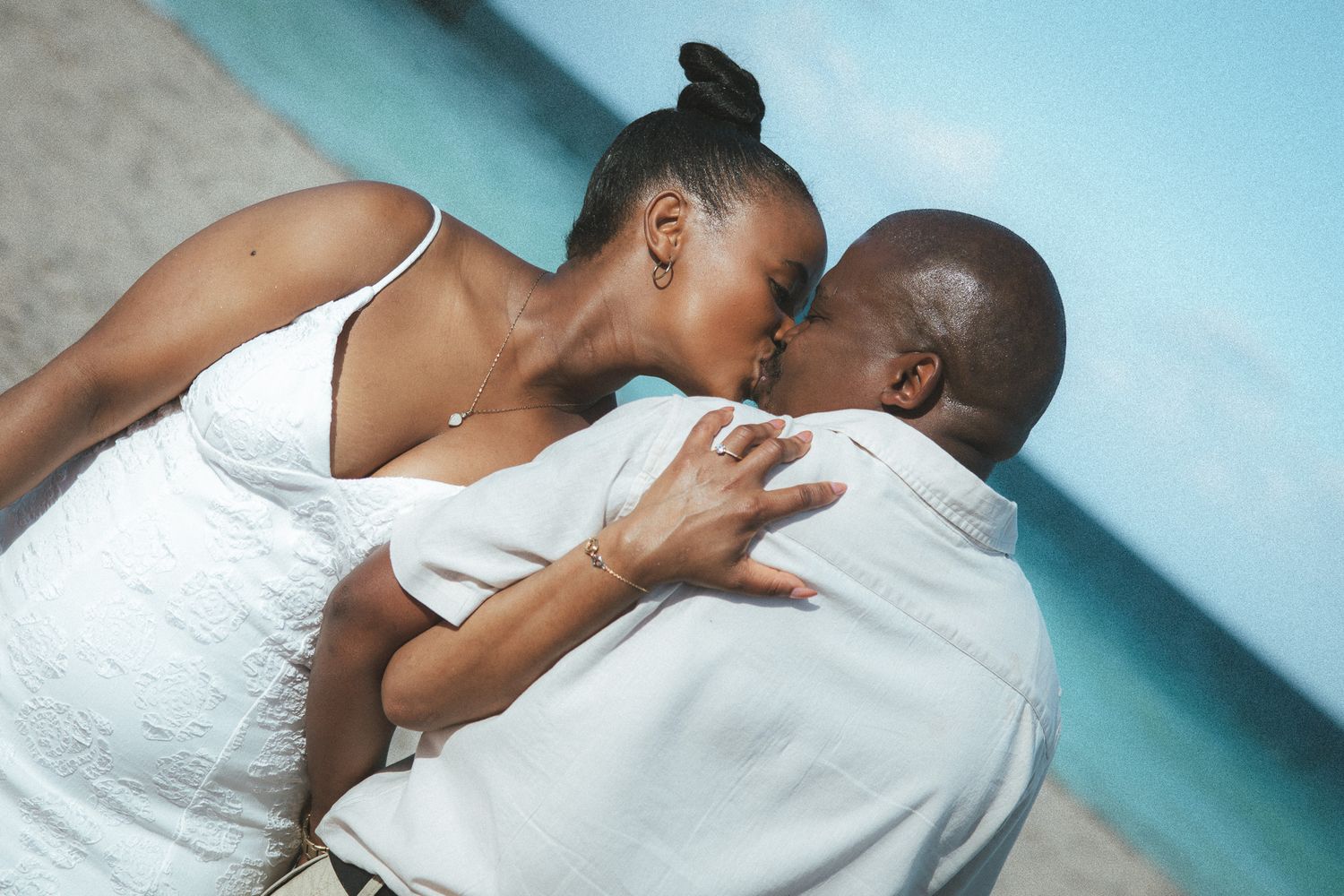 A couple sharing a passionate kiss on a beach with vibrant turquoise water visible in the background.