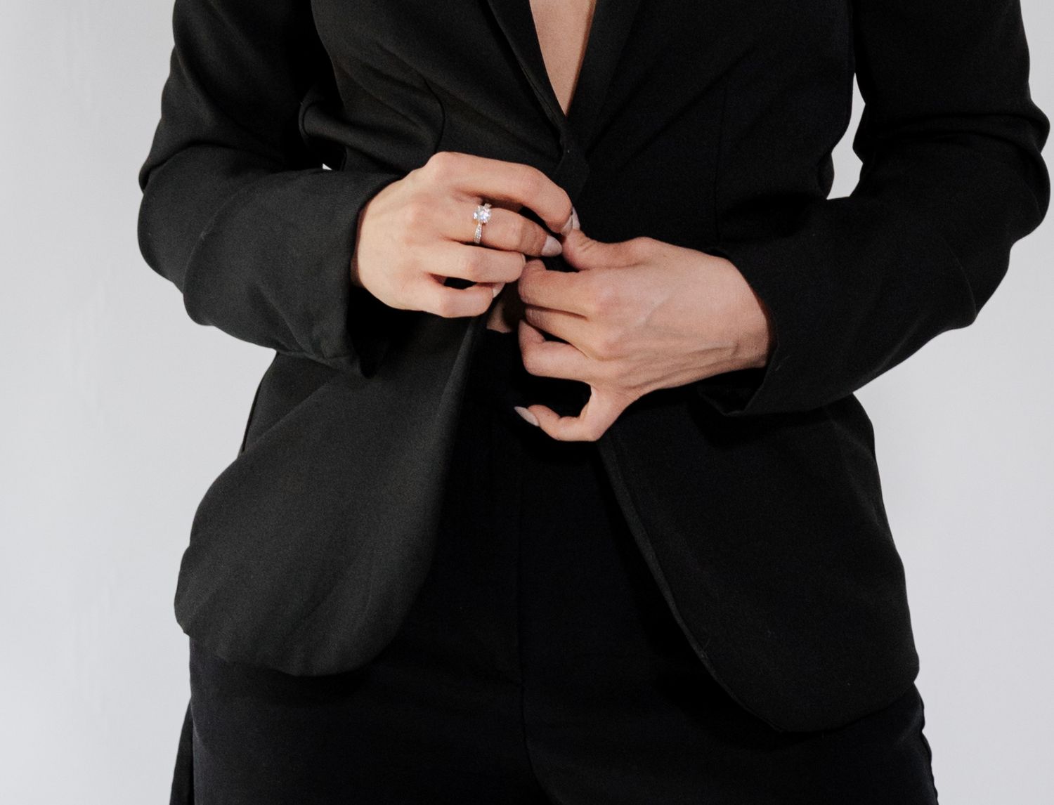Close-up of woman in black blazer adjusting buttons with diamond ring on finger.