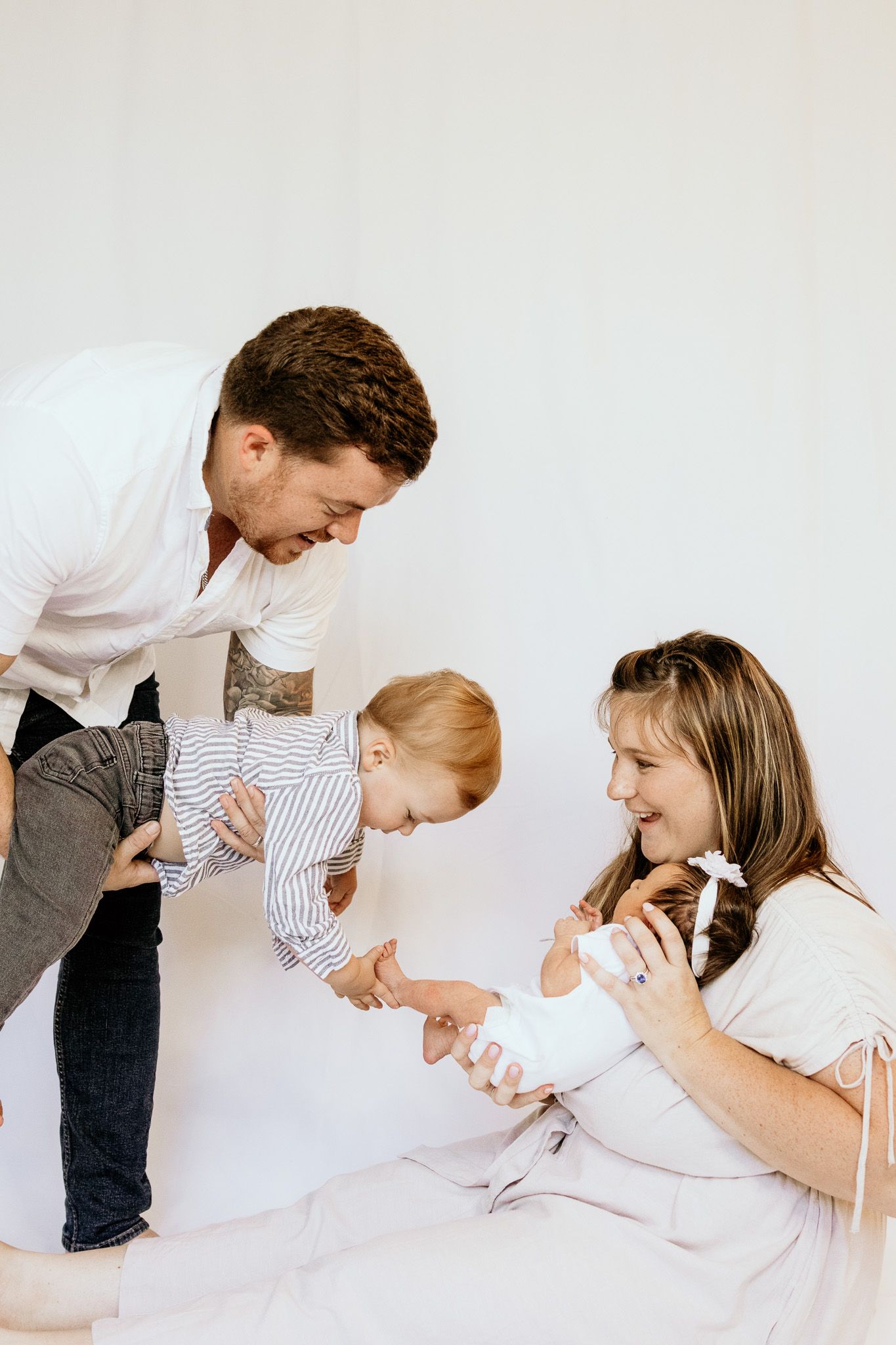 Happy family with father holding toddler and mother sitting on floor with newborn baby.