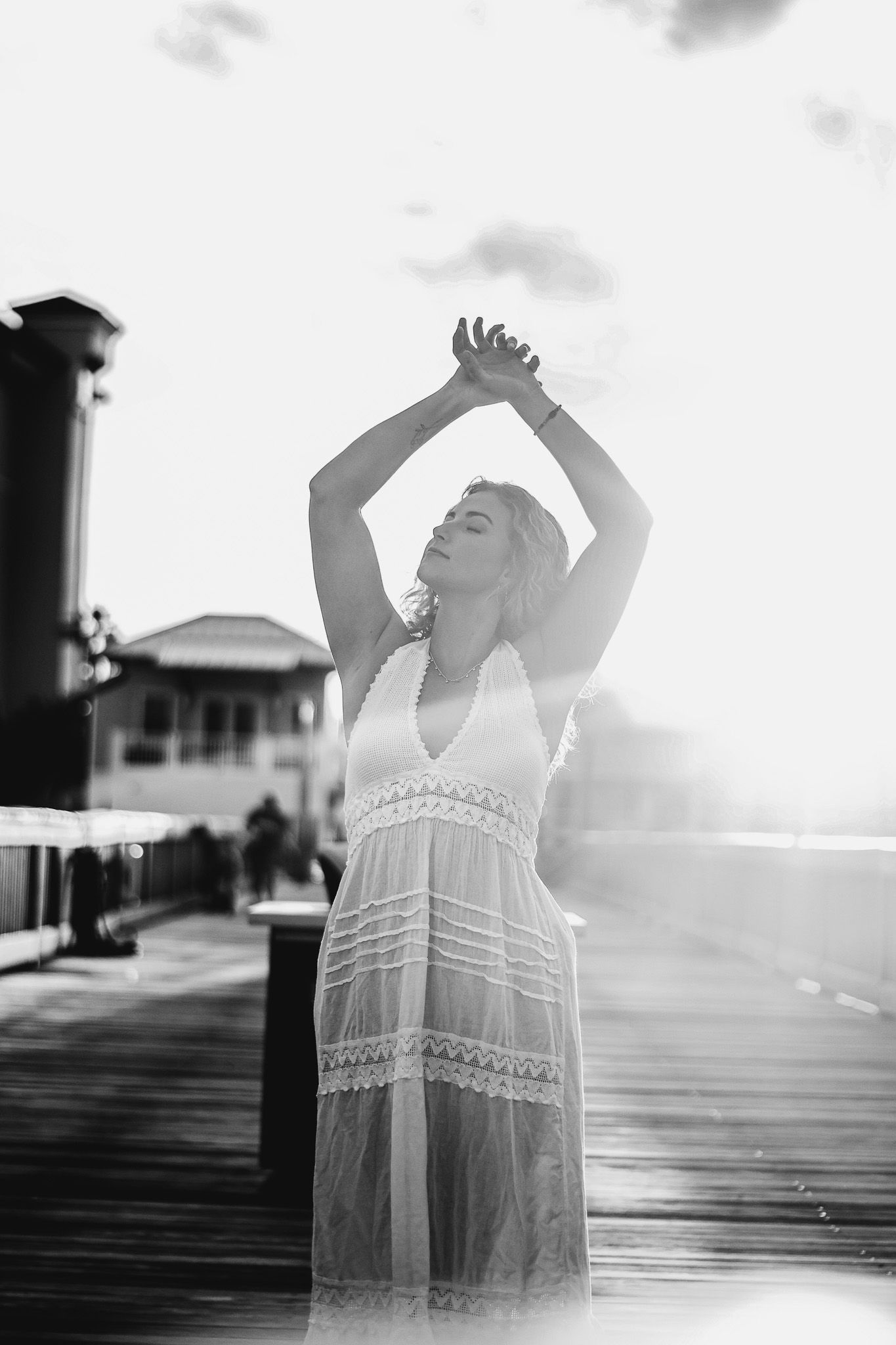 Woman in white dress arms raised on pier at sunset.