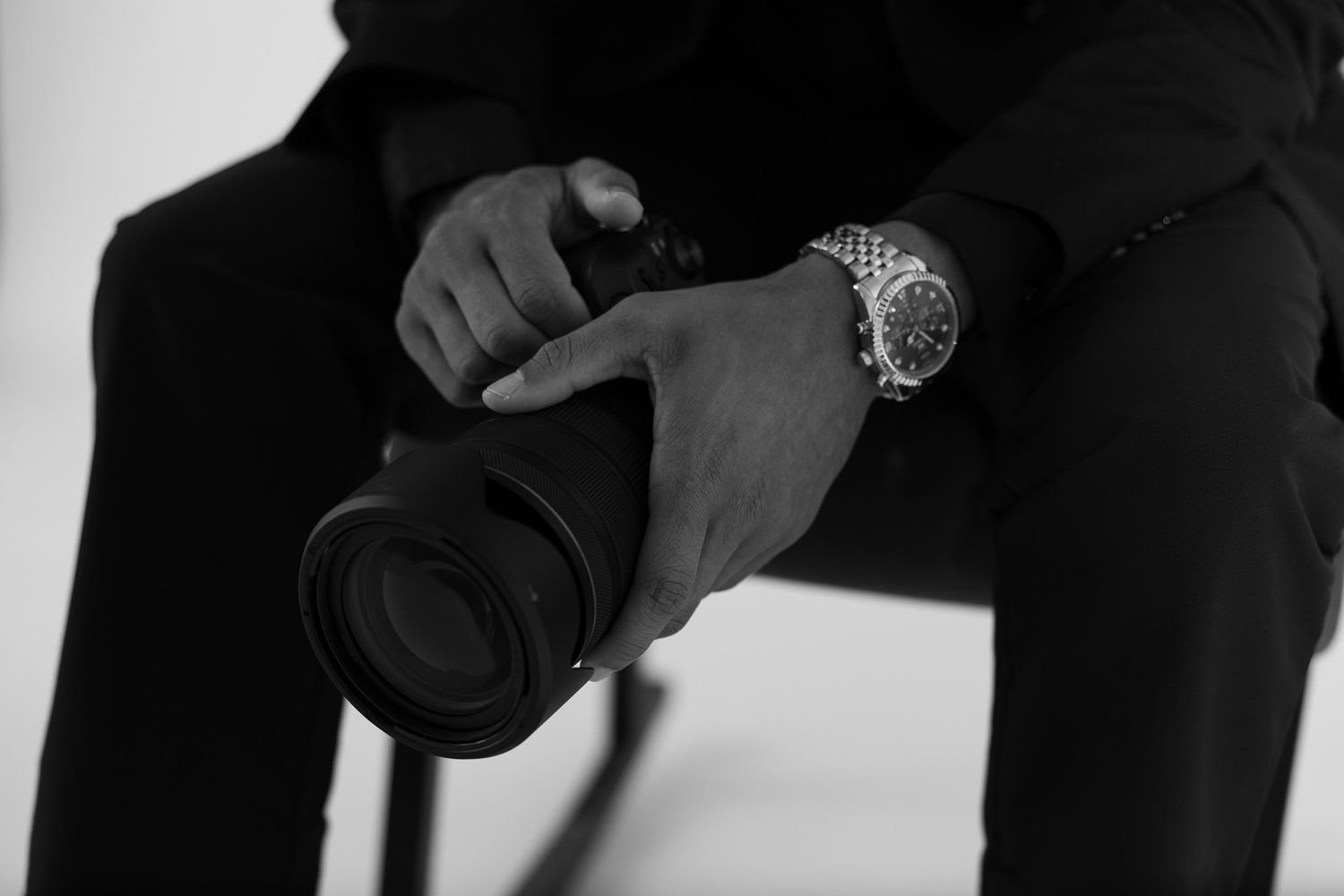 Black and white photo of a man in a suit holding a professional camera with a watch on his wrist.