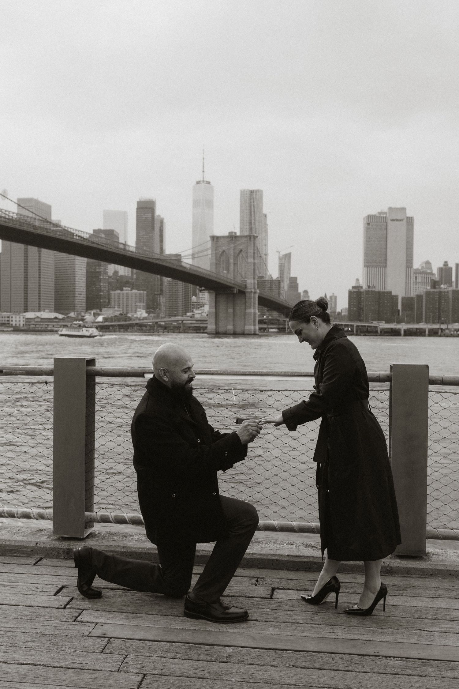 Two people sit together on a pier overlooking the Manhattan skyline and East River.