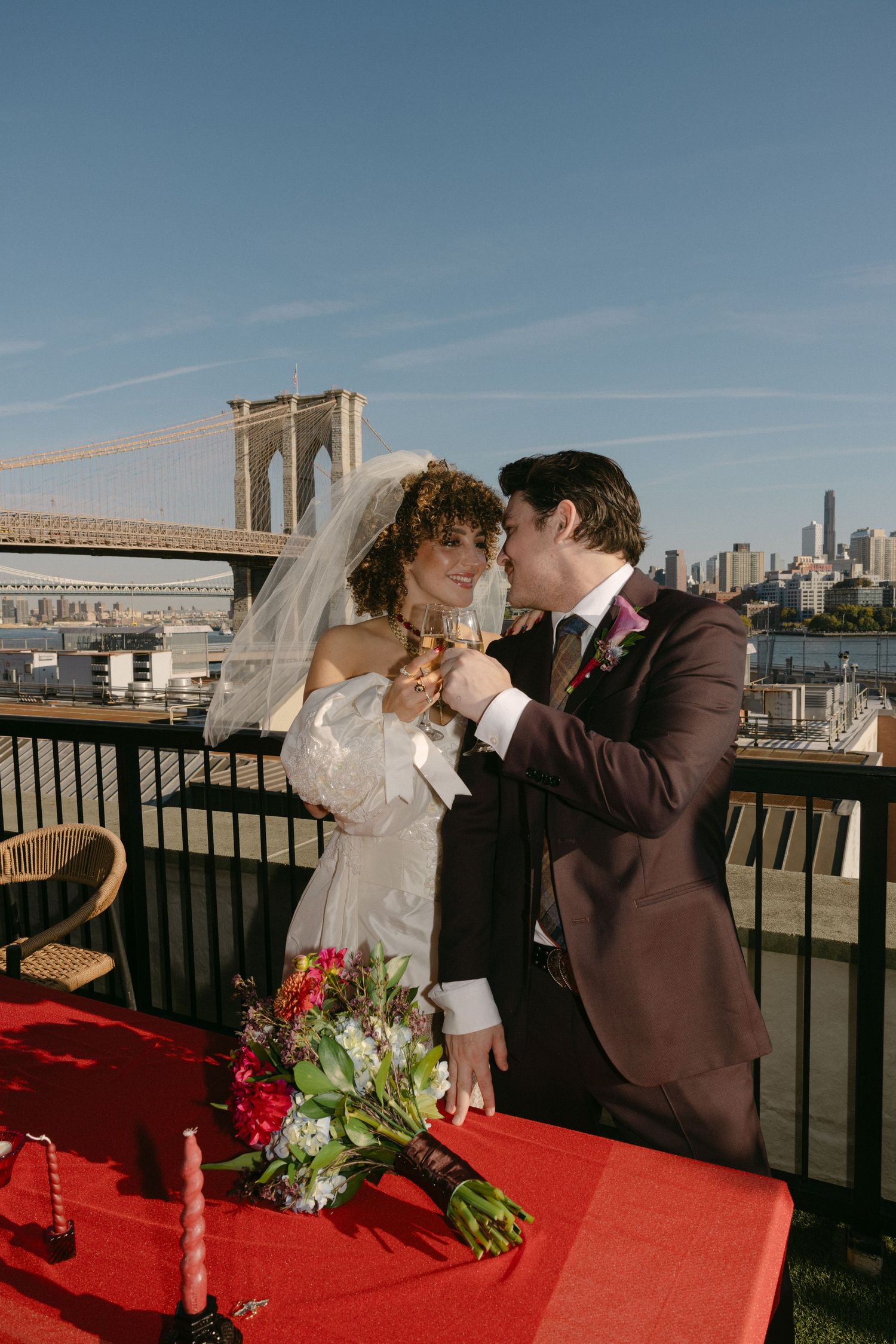 Wedding couple sharing intimate moments on a rooftop with Brooklyn Bridge in background.
