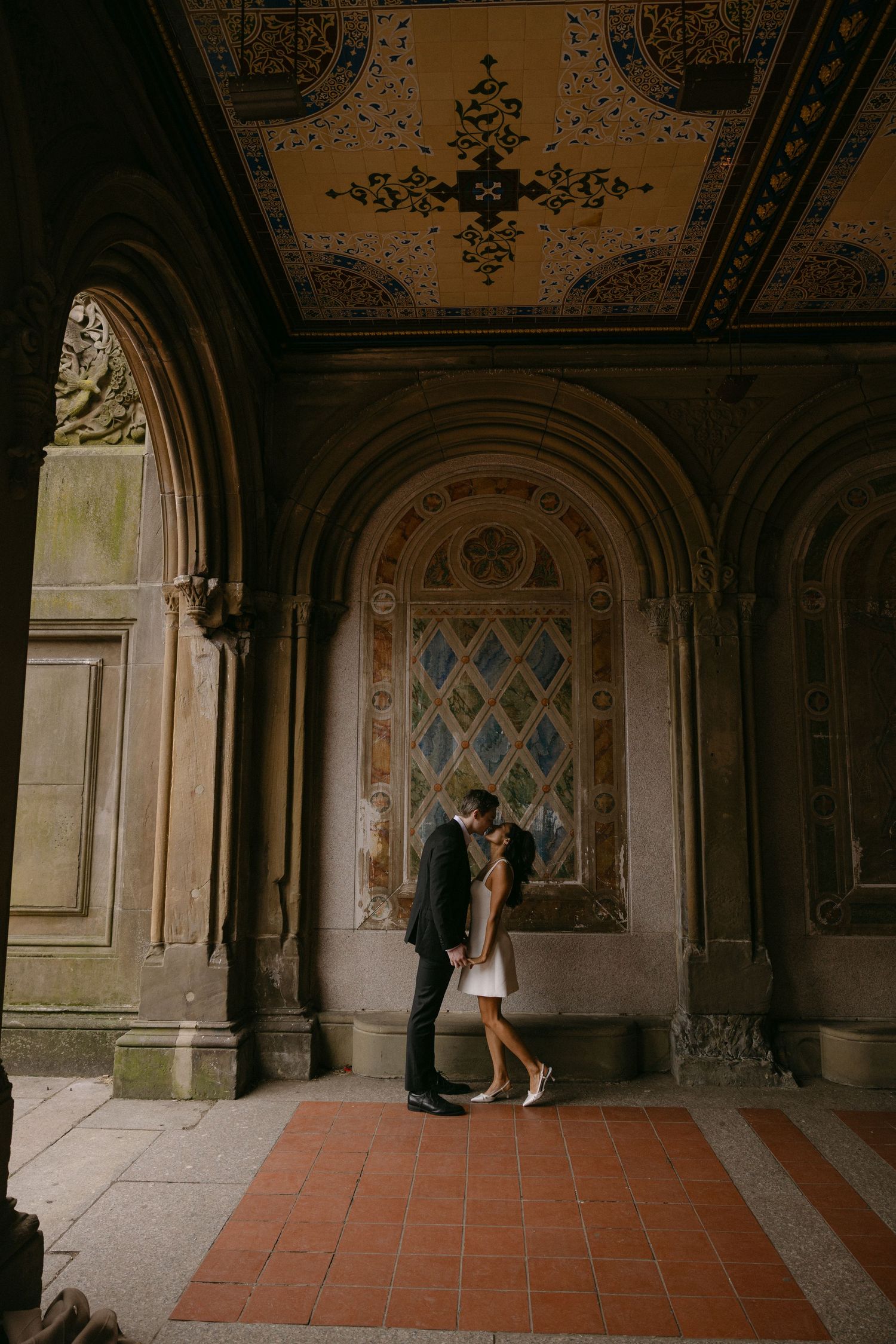 A romantic photoshoot in an ornate architectural passageway with terracotta floors and decorative arches.