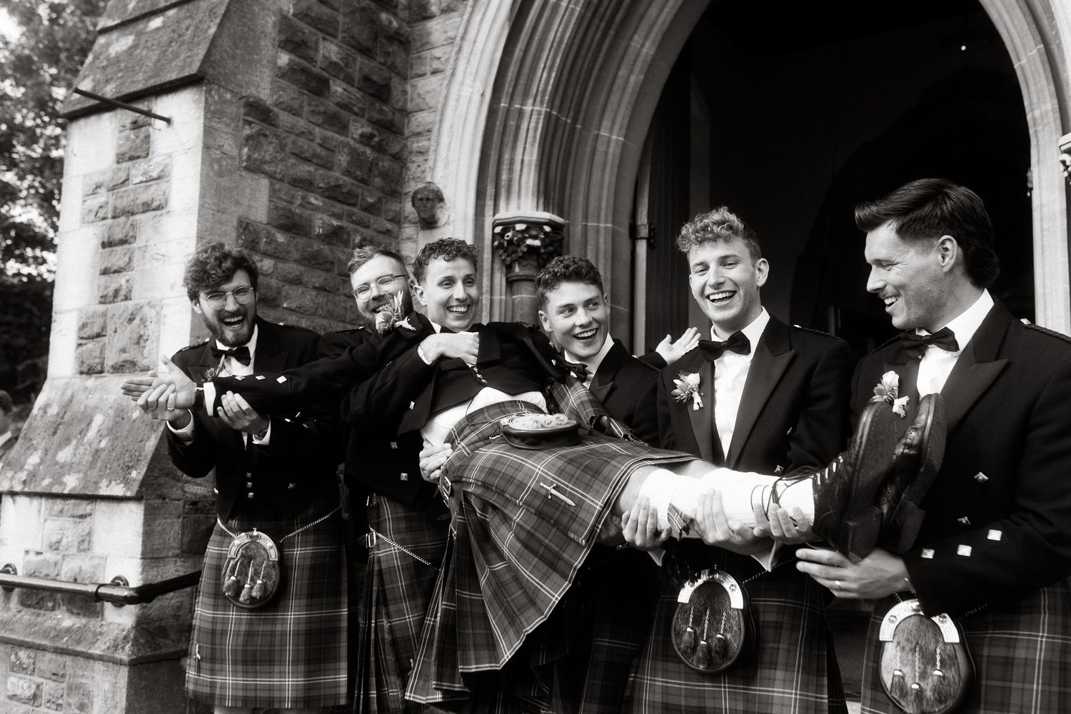 Wedding party members standing outside a stone church entrance in formal attire.