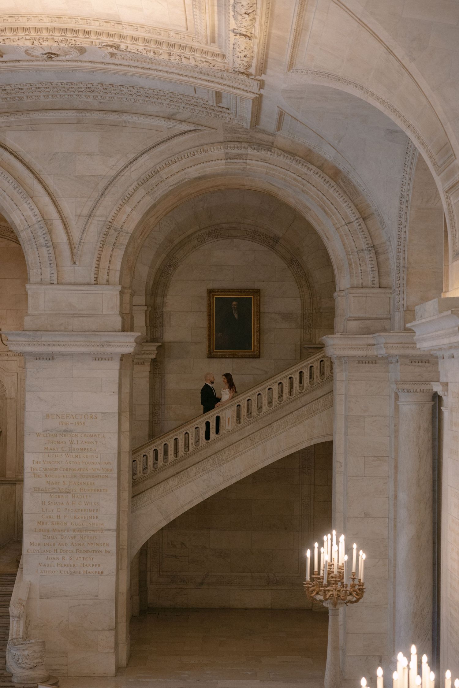 Ornate white marble staircase with arched colonnade and chandeliers in a grand classical interior.