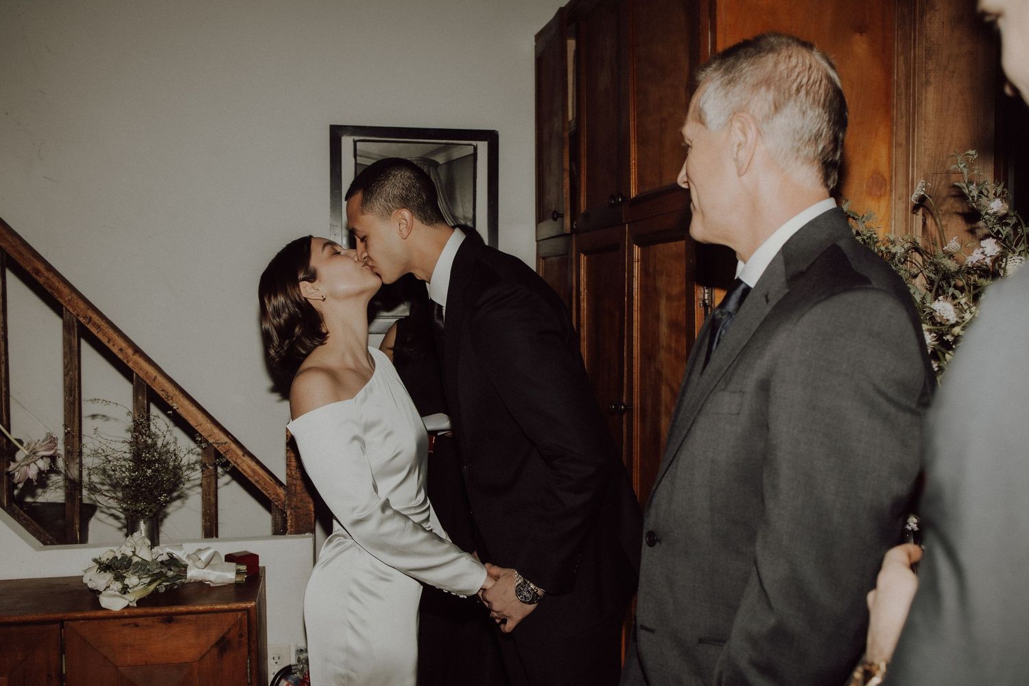 Wedding guests gather in a wood-paneled hallway during a celebration.