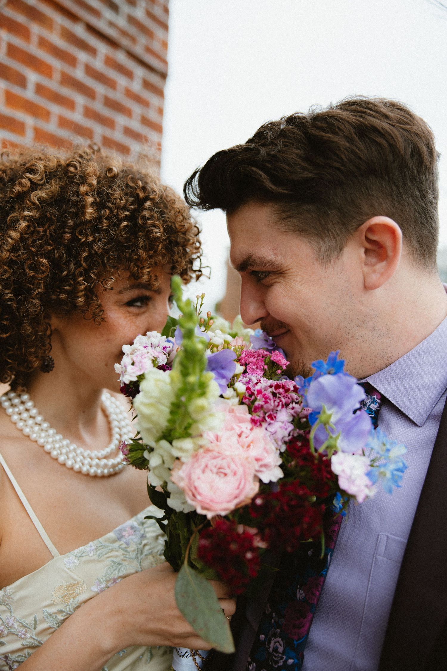 Close-up of couple with colorful wedding bouquet featuring pink and purple flowers.