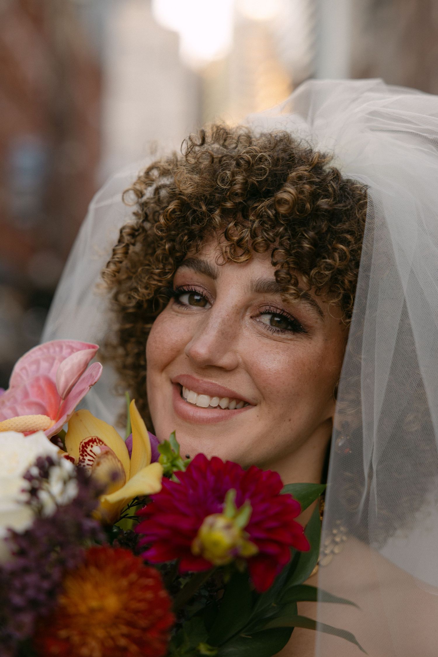 Close-up sequence of bride with curly hair and veil holding colorful wedding bouquet.