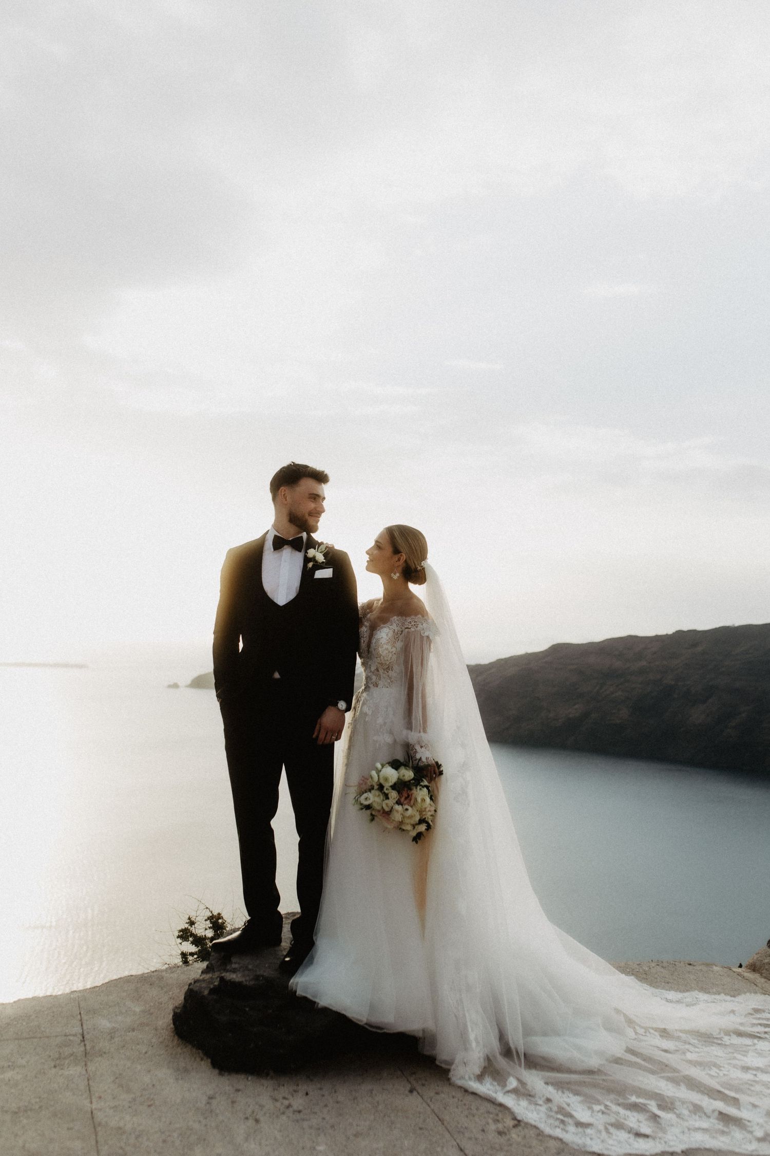A romantic wedding couple poses on a scenic cliff overlooking a serene lake on their special day.