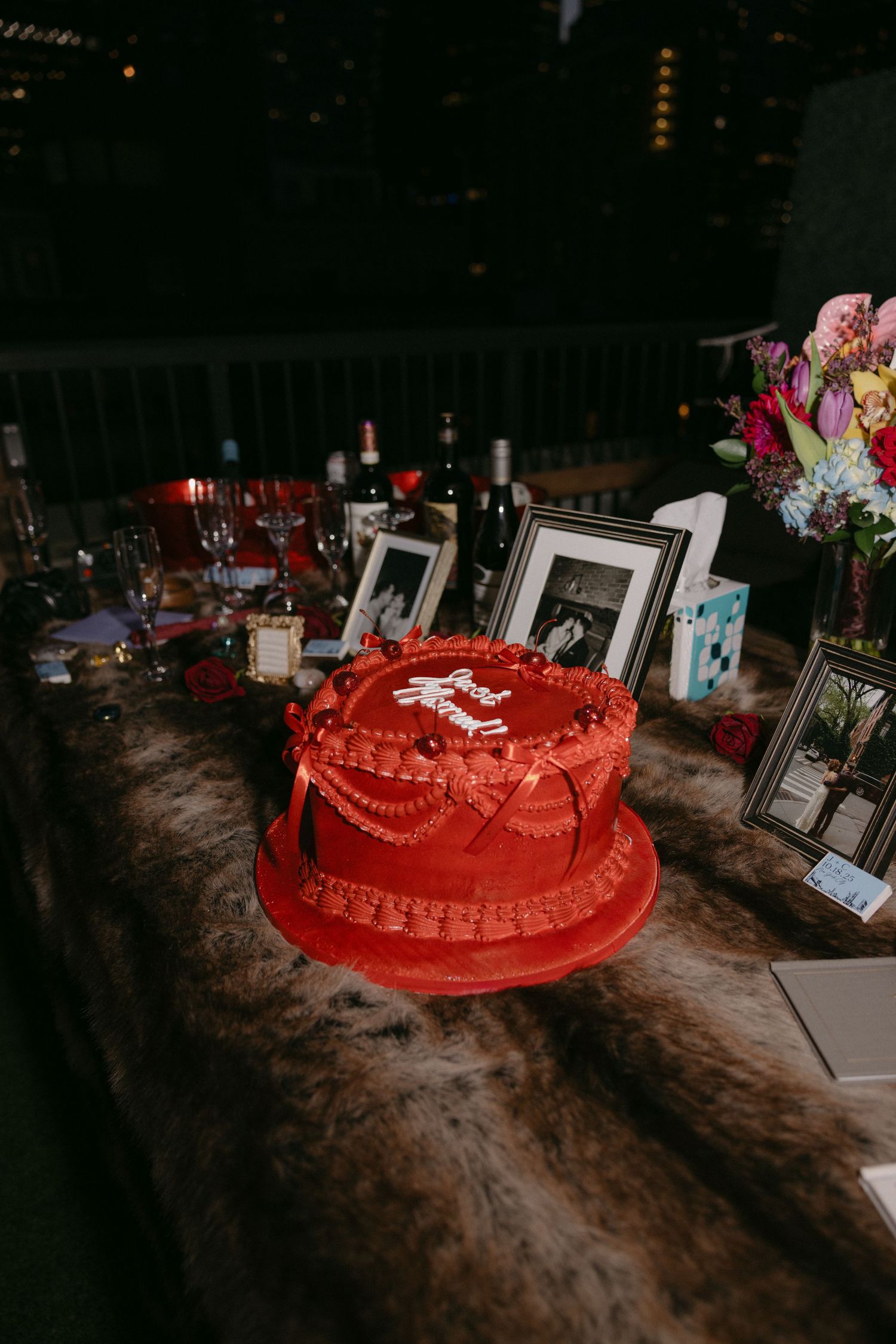 A red wedding cake with white decorative details sits on a dark wooden table at a reception venue.