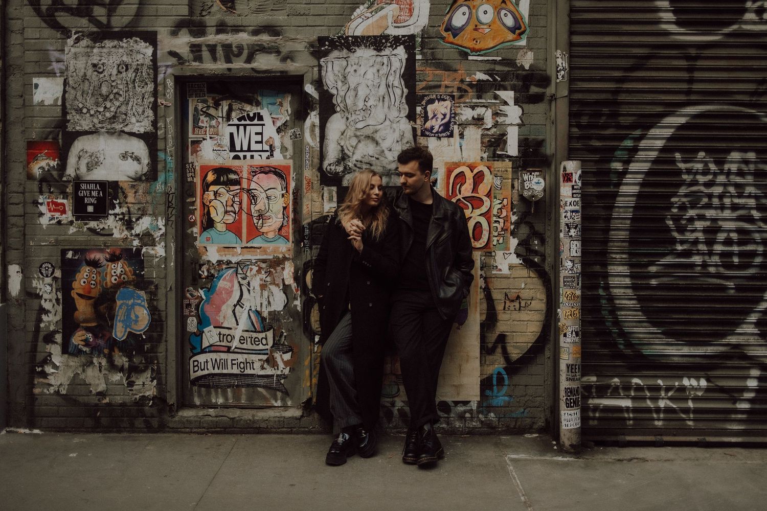 Urban couple portrait against graffiti covered wall in moody lighting.