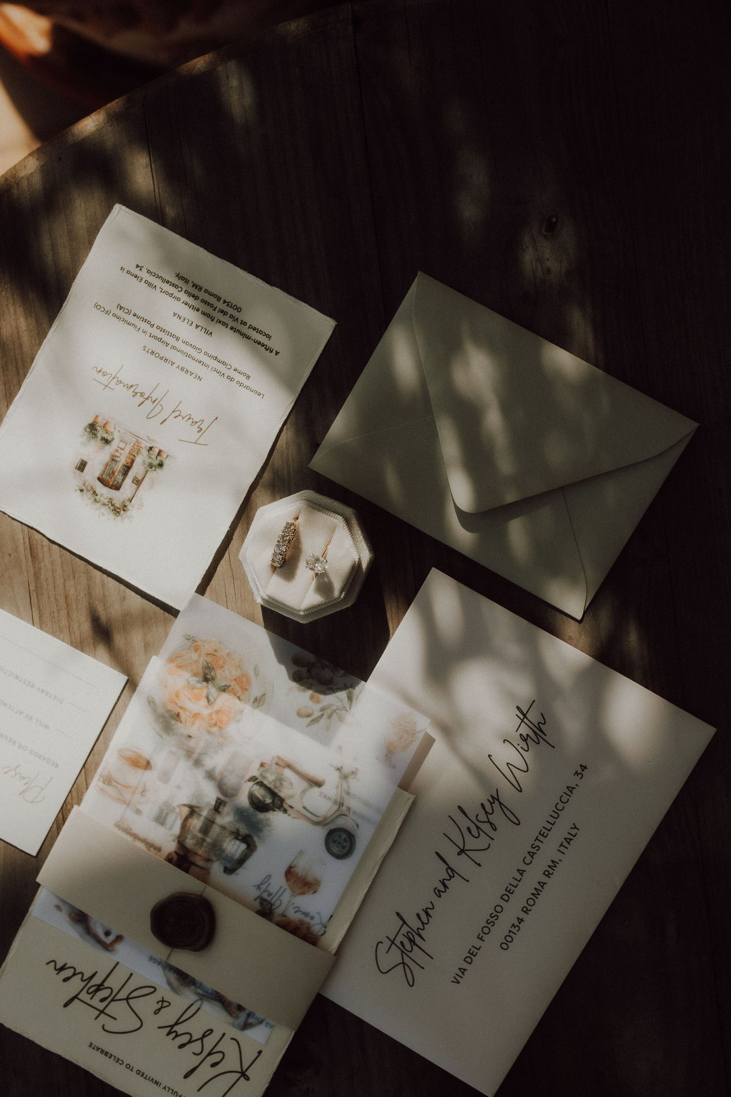 Wedding invitation suite with envelopes and stationery arranged on wooden surface in moody lighting.