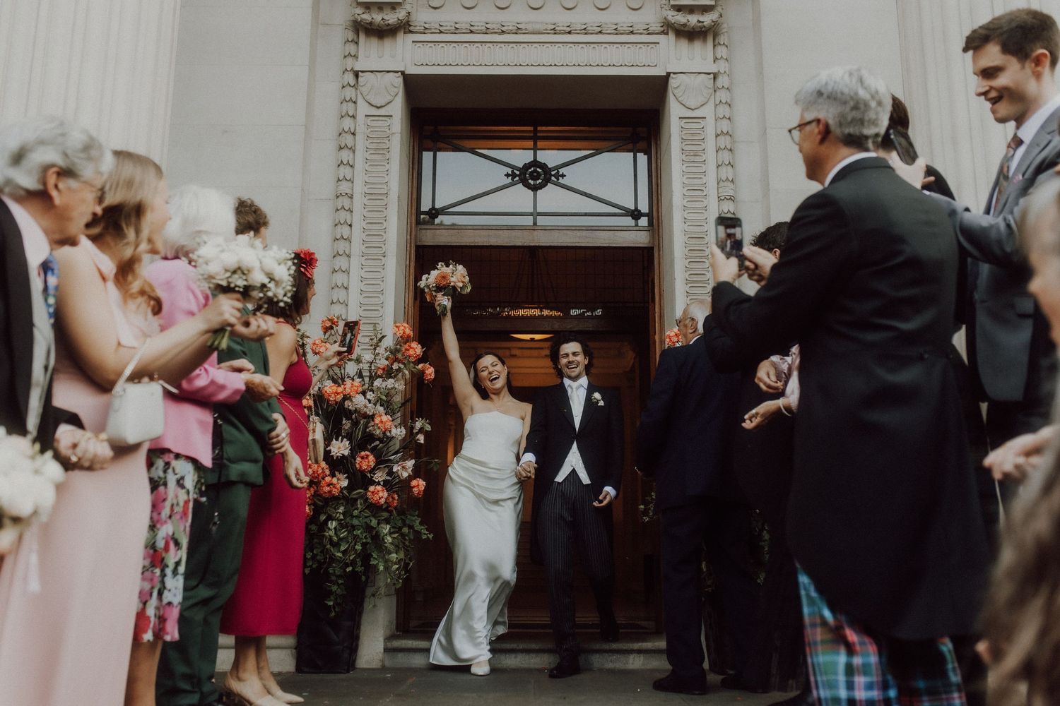 Wedding guests gathering outside elegant white building entrance with classical details.
