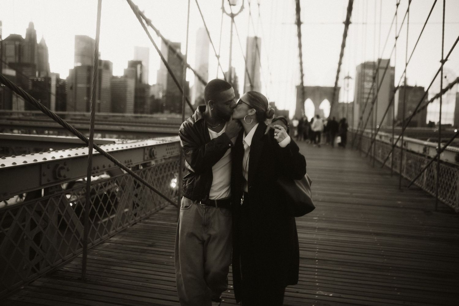 Atmospheric black and white photo on Brooklyn Bridge with NYC skyline in background.