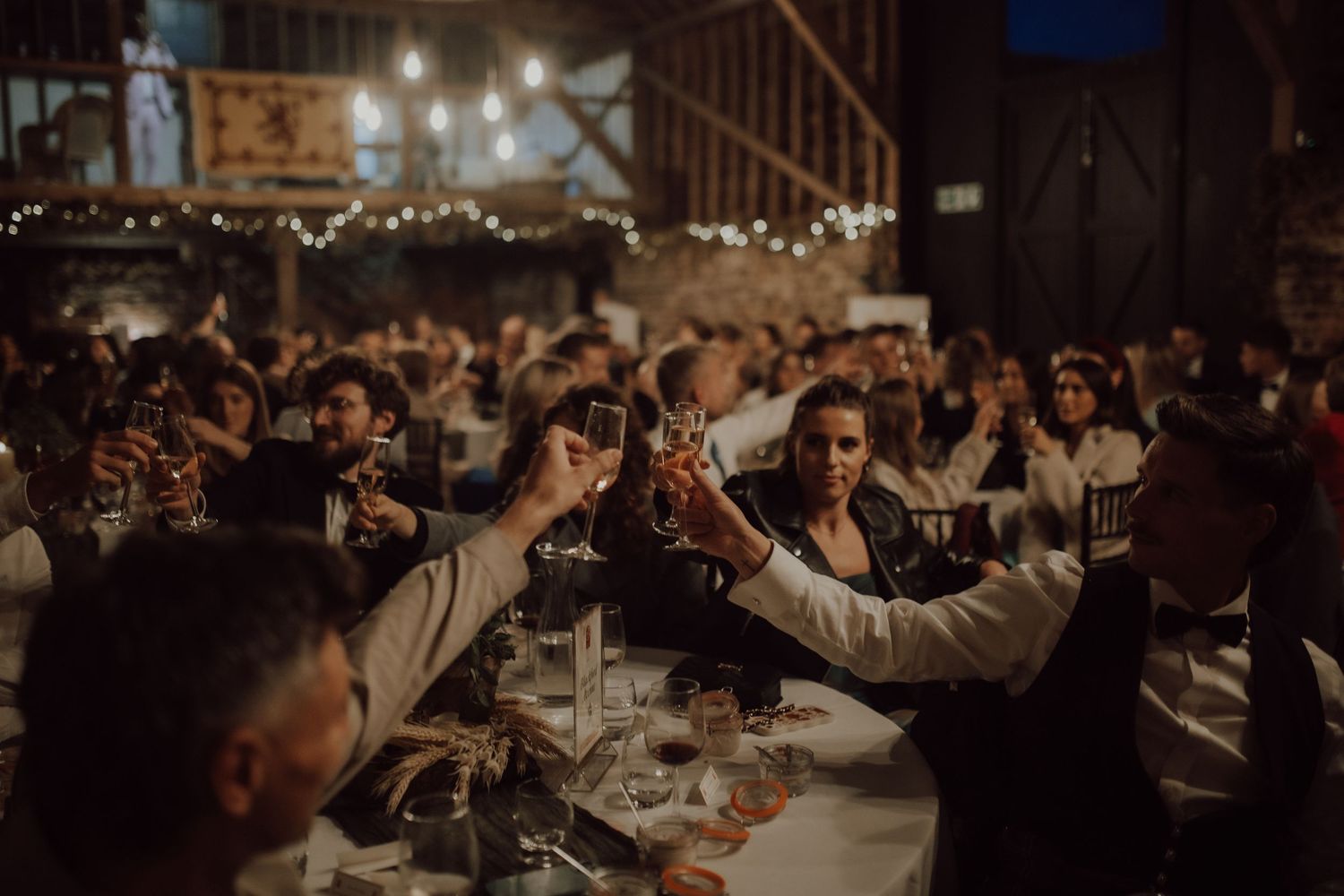 Crowded wedding celebration in a dimly lit rustic venue with exposed wooden beams.