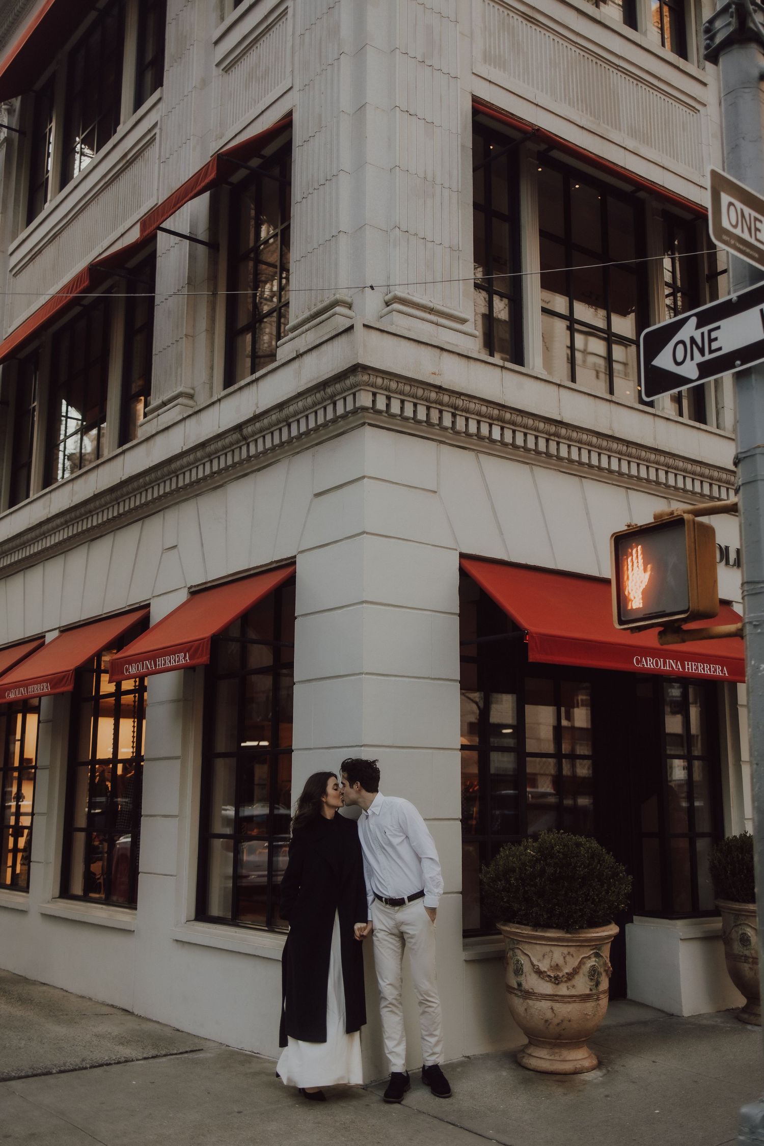 A couple stands outside a classic building with red awnings in an urban setting.