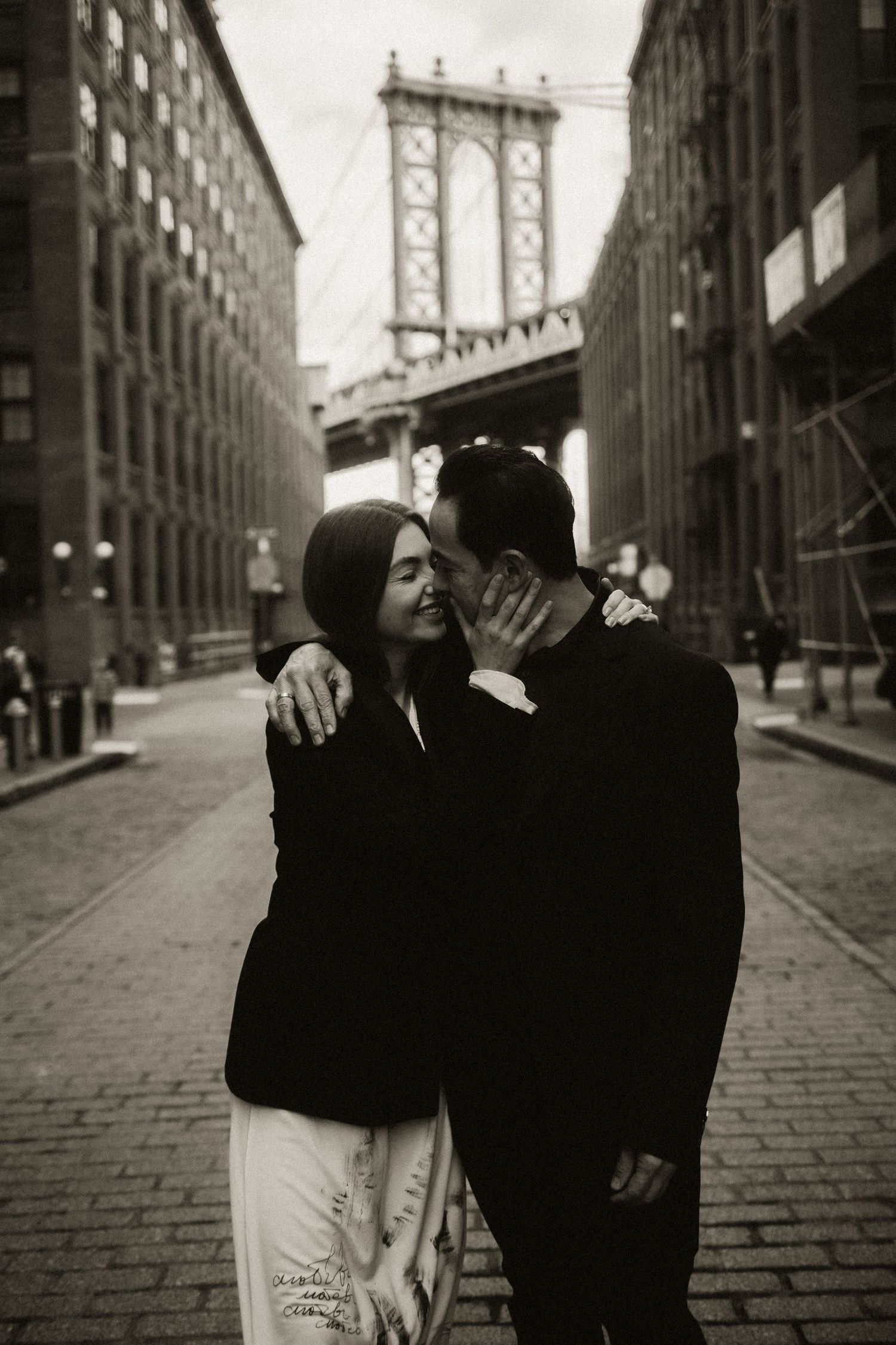 Intimate black and white portrait with Manhattan Bridge looming between industrial buildings.
