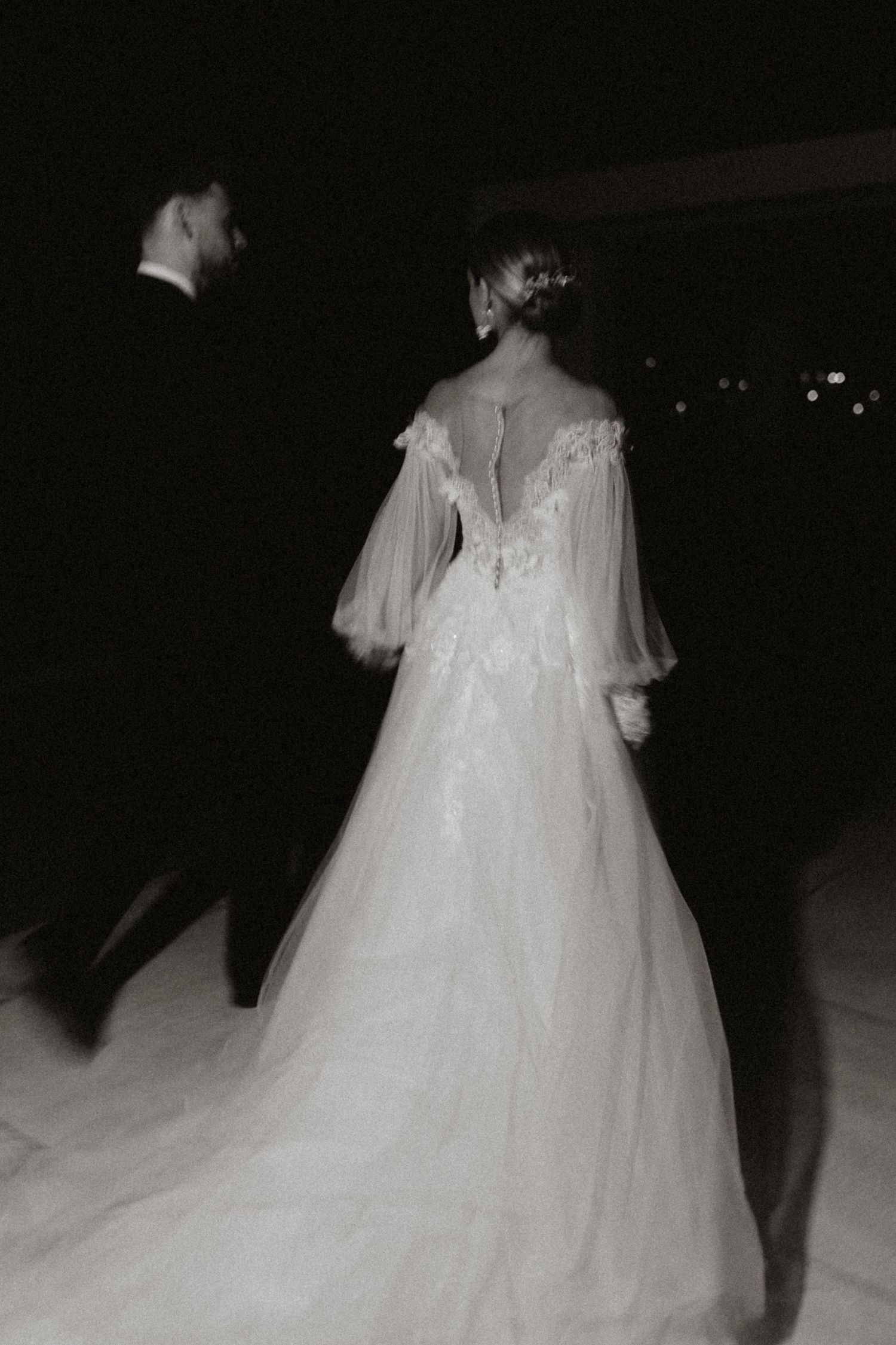 A flowing white wedding dress trails behind in dramatic black and white photography.