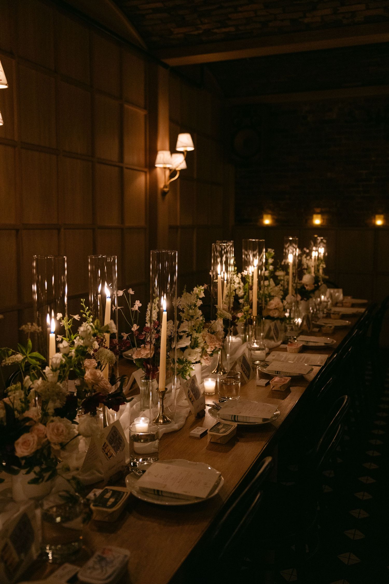 Elegant candlelit wedding reception tables decorated with white floral centerpieces and glowing taper candles in a rustic venue.