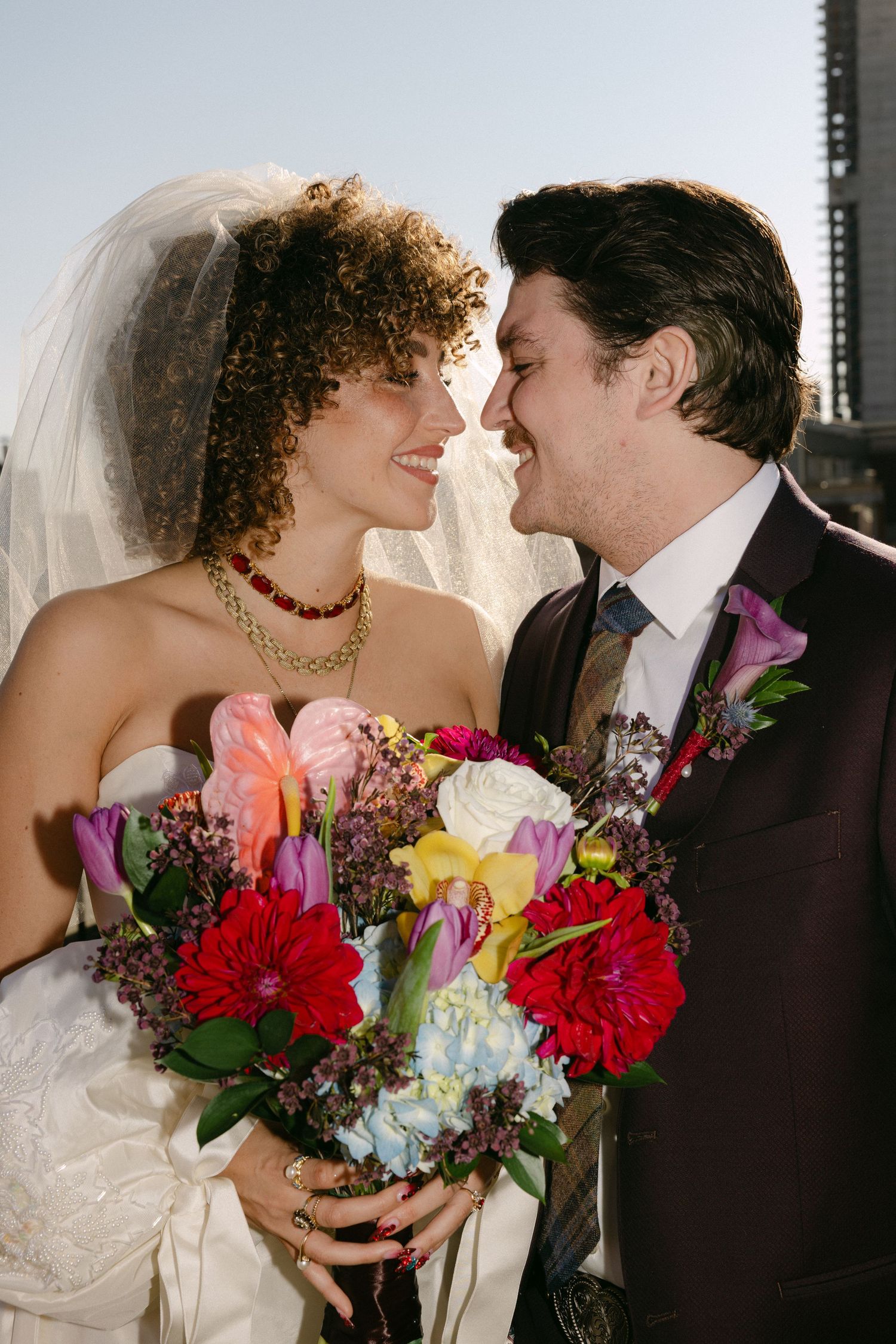 Newlyweds posing with vibrant bouquet of flowers against city backdrop.