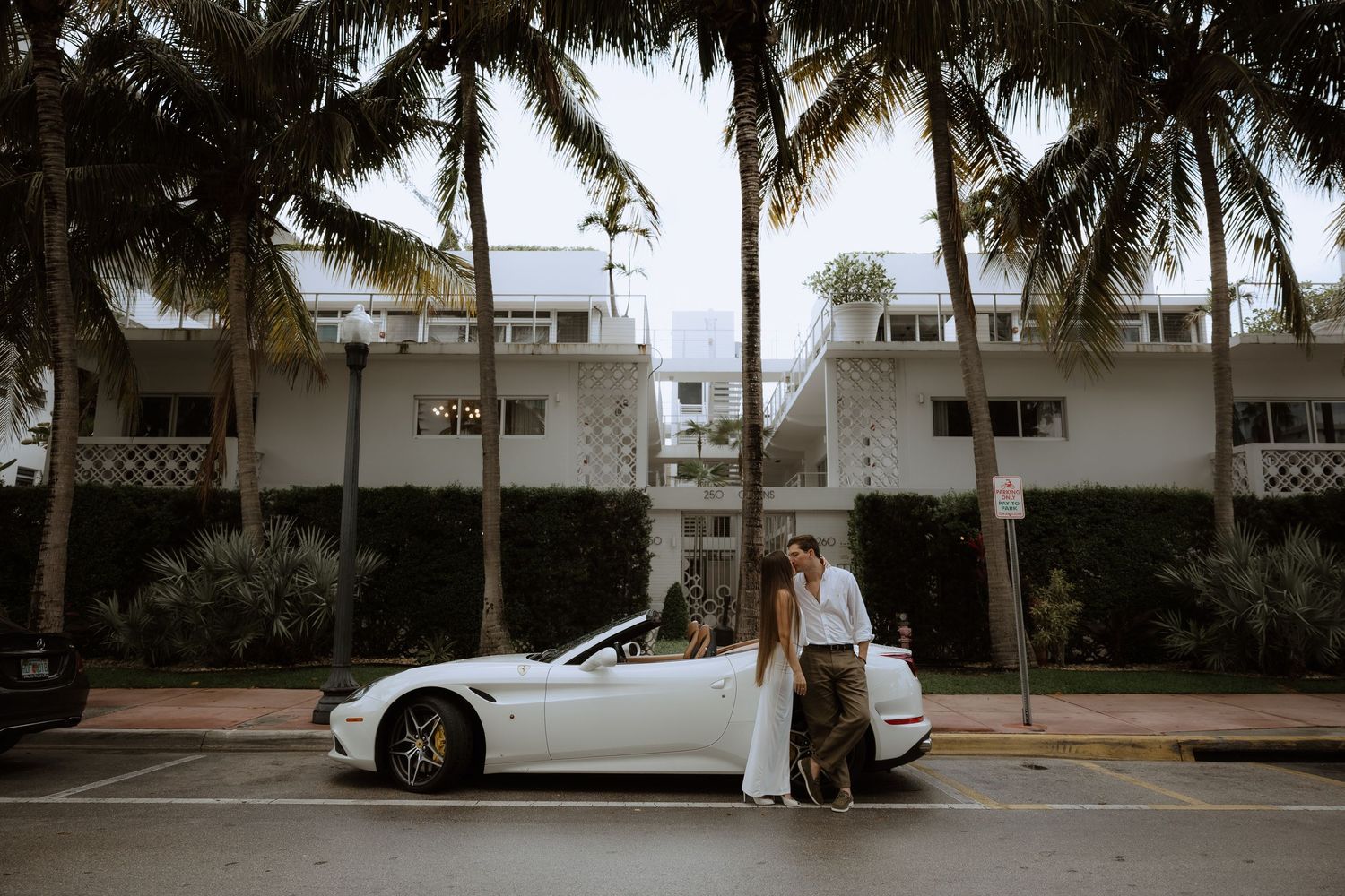 A white car parked near palm trees on a tropical street.