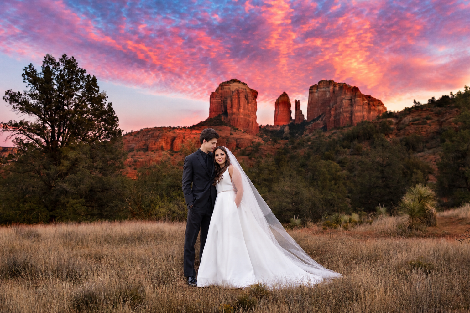 Bride and groom embrace at sunset in Sedona with Cathedral Rock and vibrant pink sky backdrop.