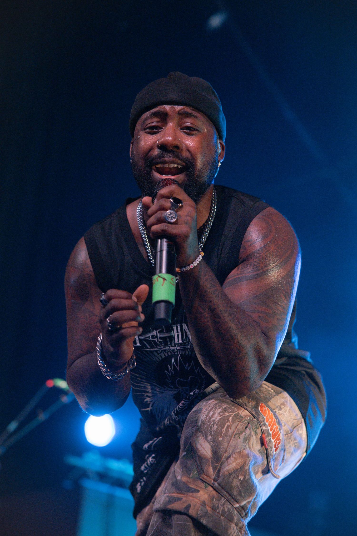 Musician performer singing passionately on stage with dramatic blue lighting and visible tattoos on arm.