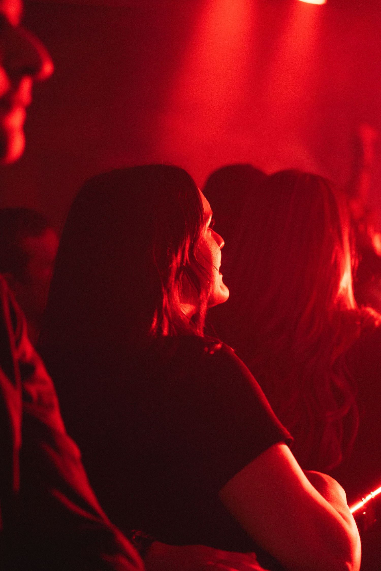 Concert audience silhouettes lit by bright red stage lighting creating an atmospheric crimson glow.