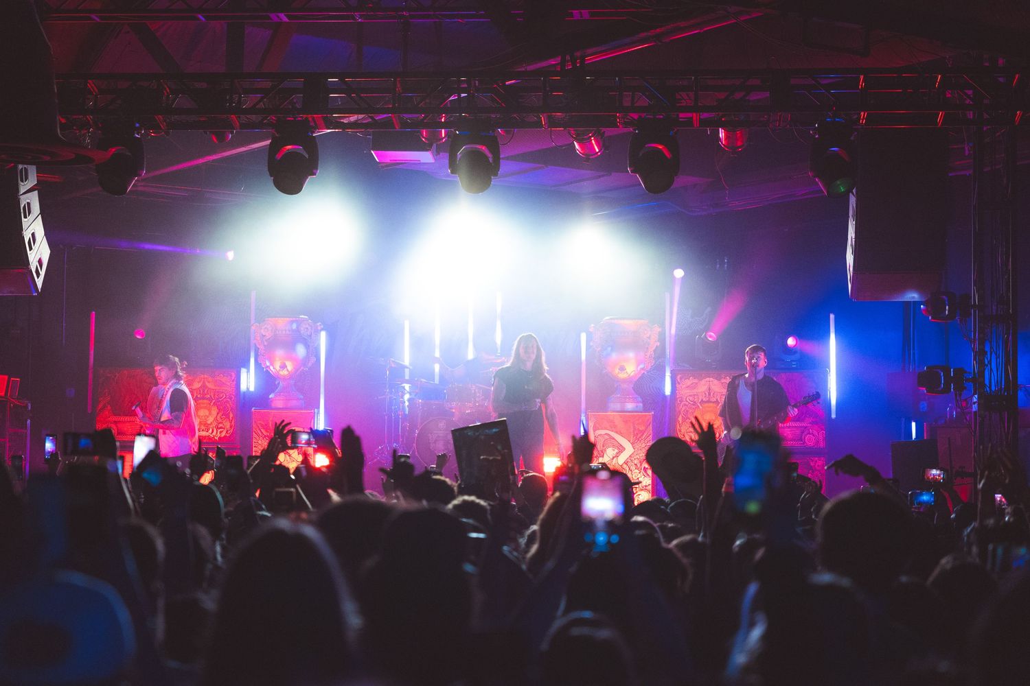 Concert crowd silhouette in front of illuminated stage with colorful red and blue lighting effects during live performance.