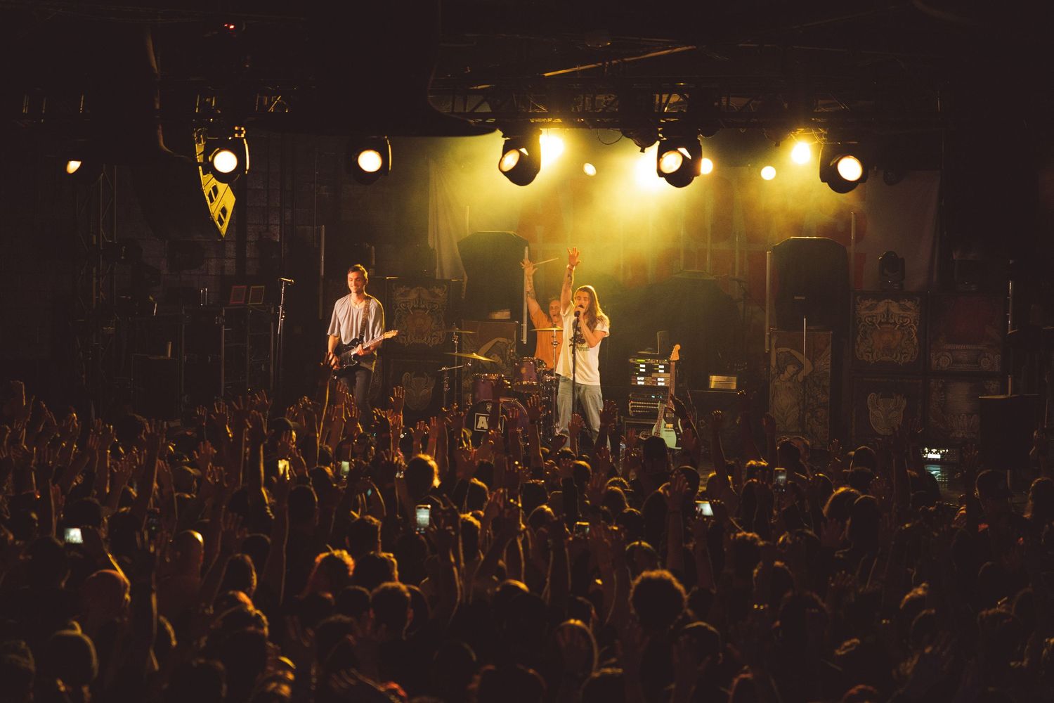 Concert venue with stage lights illuminating performers and silhouetted crowd in the foreground.