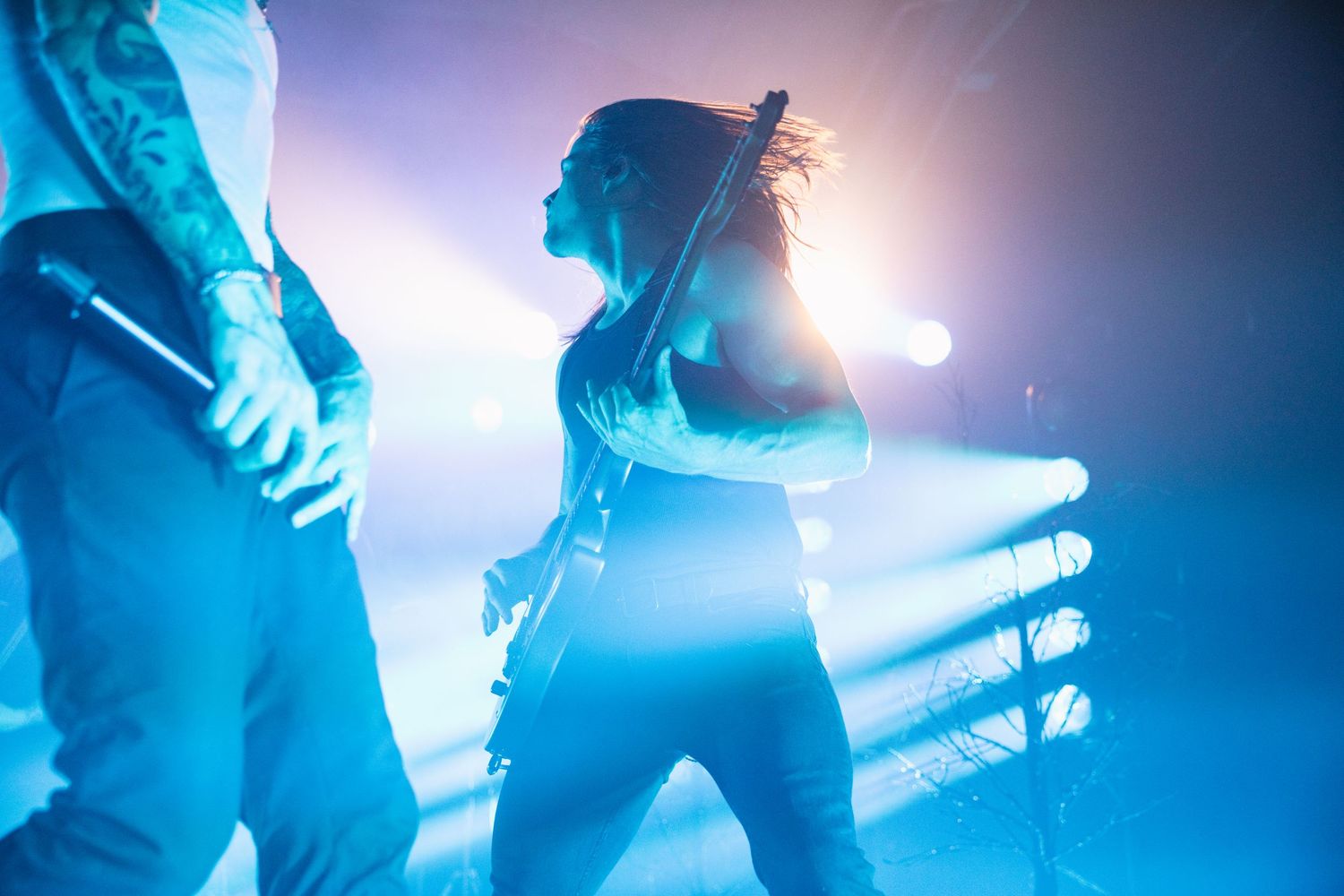Musicians perform on stage with dramatic blue lighting and silhouettes creating an atmospheric concert environment.