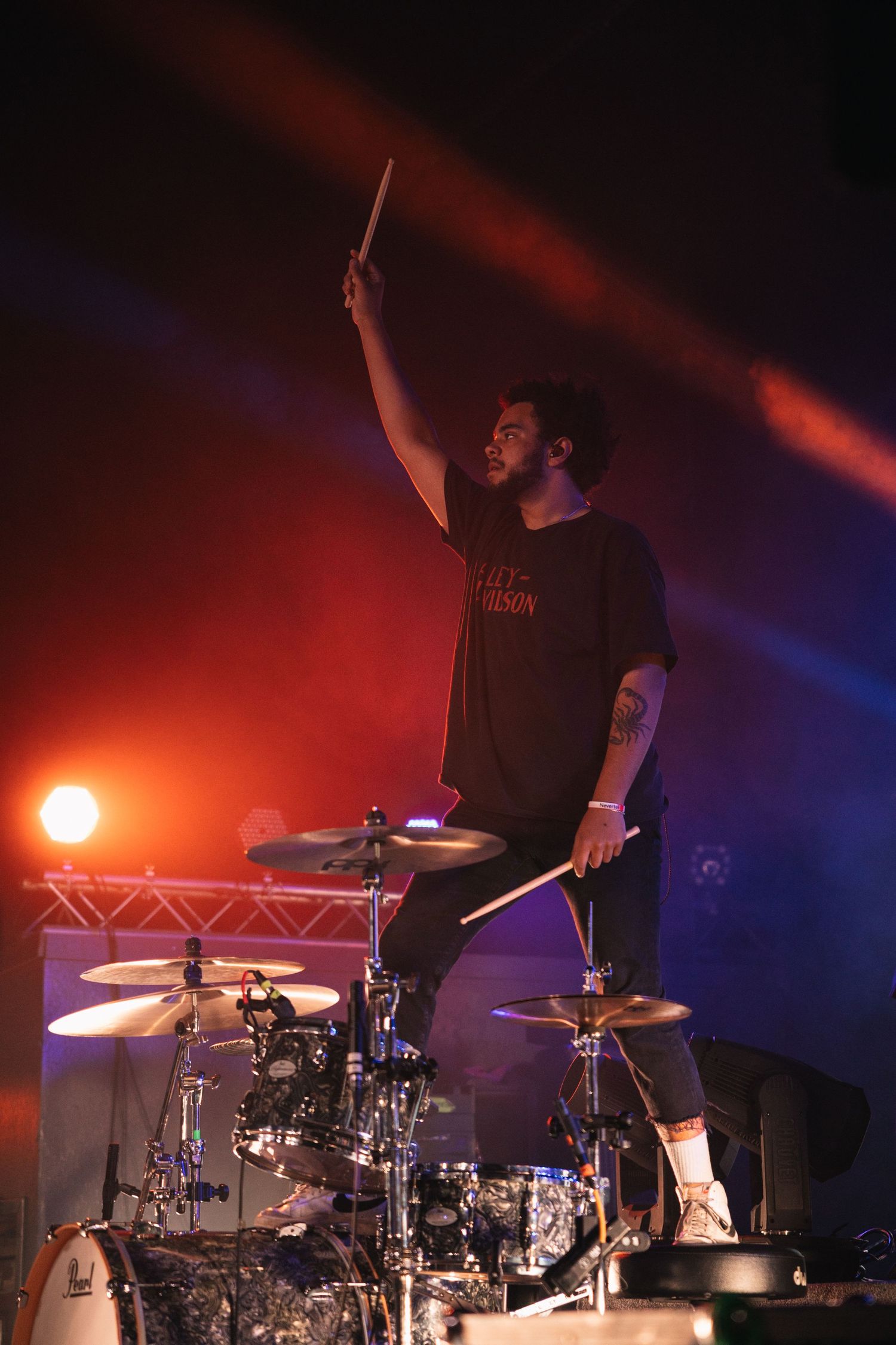 Silhouetted drummer performing on stage under dramatic red and blue lighting during a live concert performance.