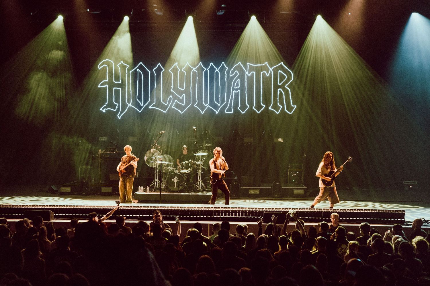HOLYWATR band performing live on stage with dramatic lighting and a large crowd at a rock concert.