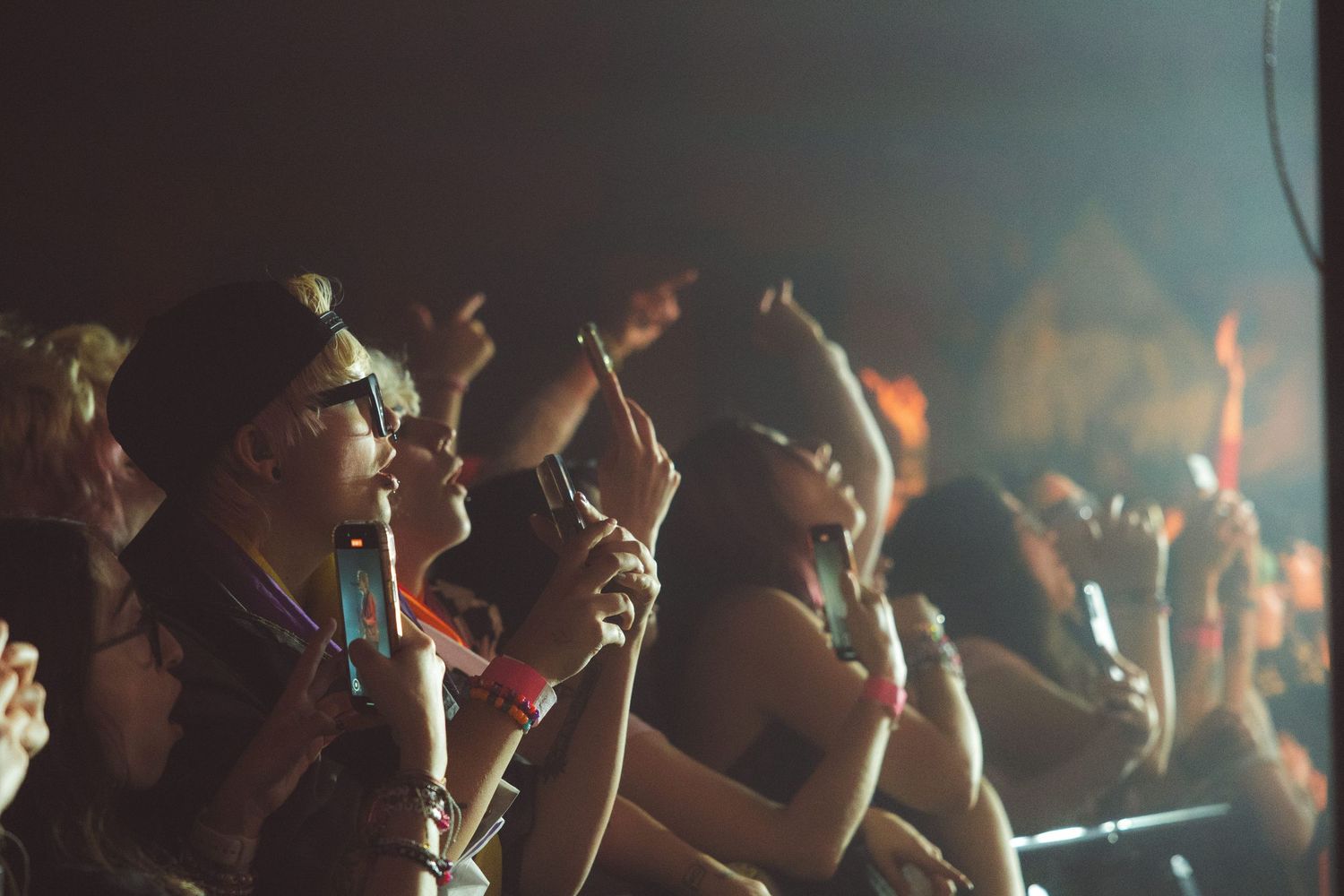 Concert crowd raises their hands in the air at a dimly lit music venue during a live performance.
