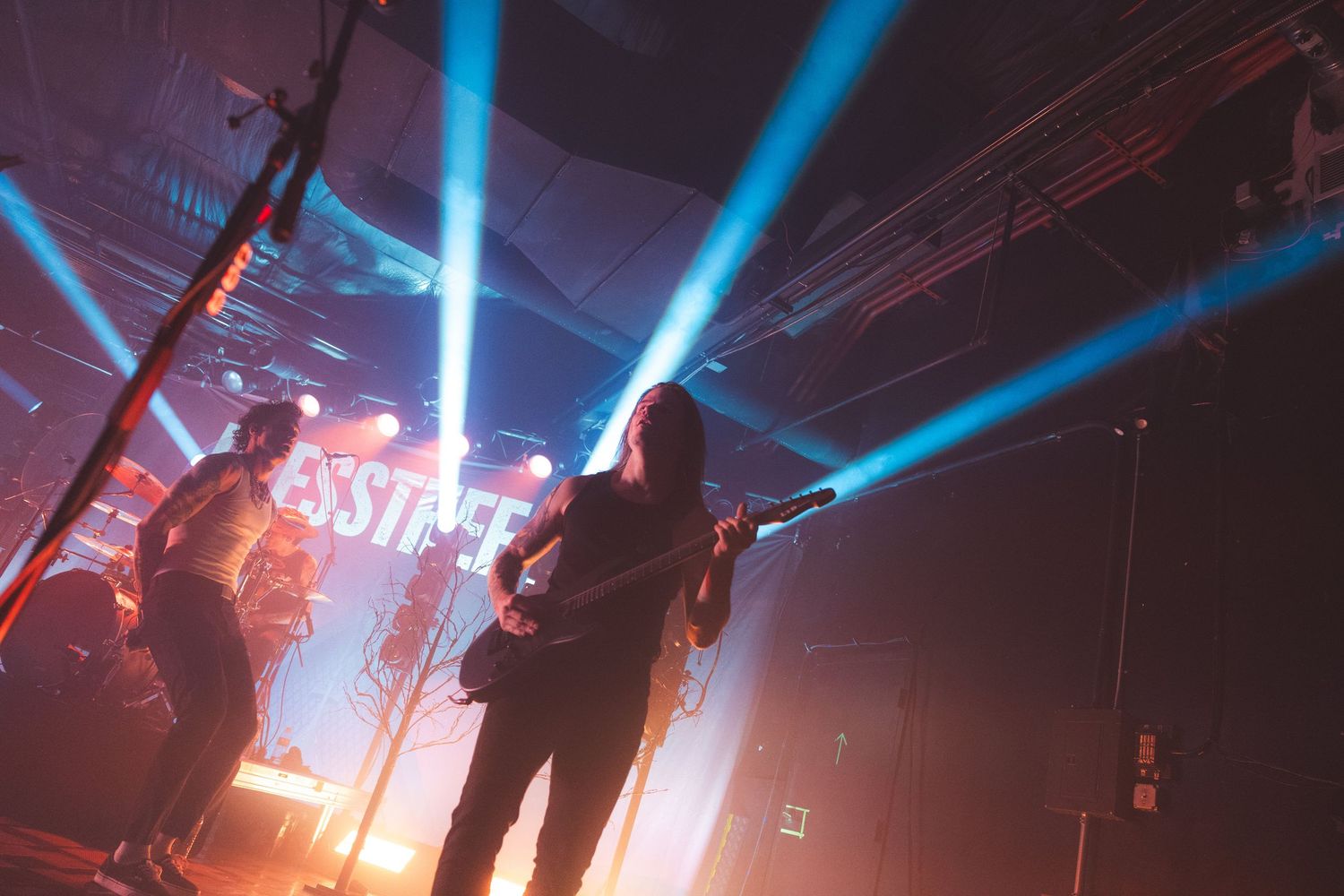 A silhouetted figure performs on stage with dramatic blue lighting and effects at a concert venue.