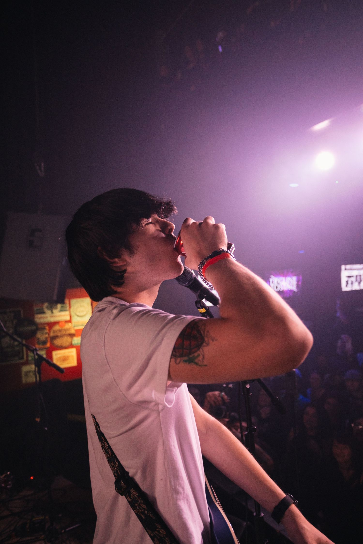 A performer in a white shirt silhouetted against purple stage lighting during an energetic concert performance.