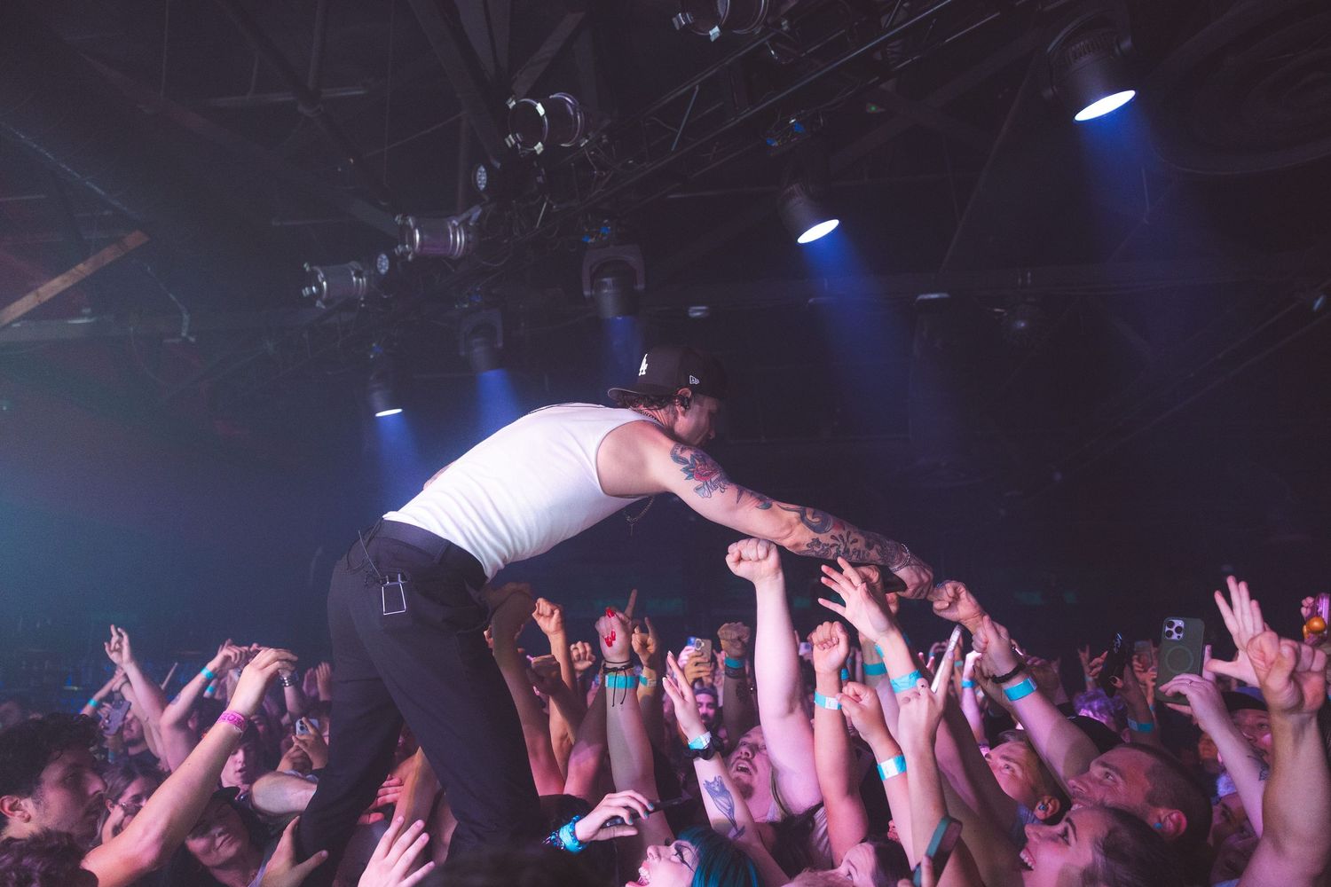 Concert crowd raises hands in the air during energetic performance with blue stage lighting and silhouetted audience.