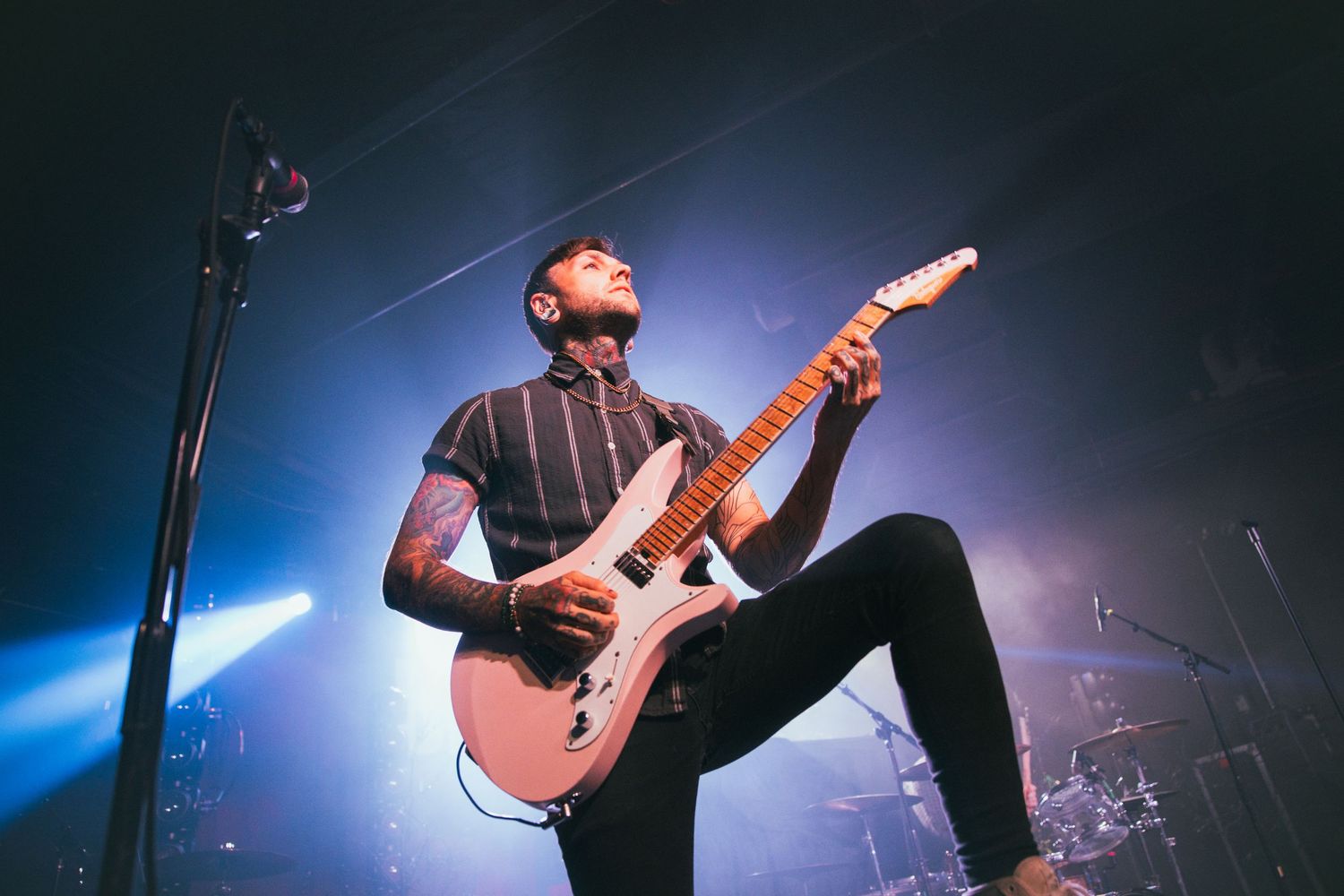 Rock musician performs under dramatic blue stage lighting with an electric guitar during energetic concert performance.