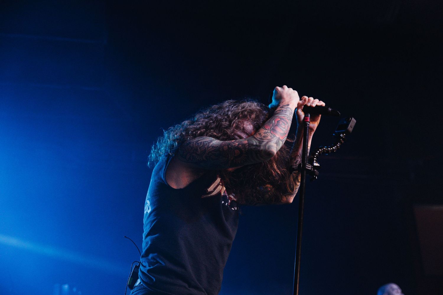 Silhouetted performer sings on dark stage with dramatic blue lighting effects in background.