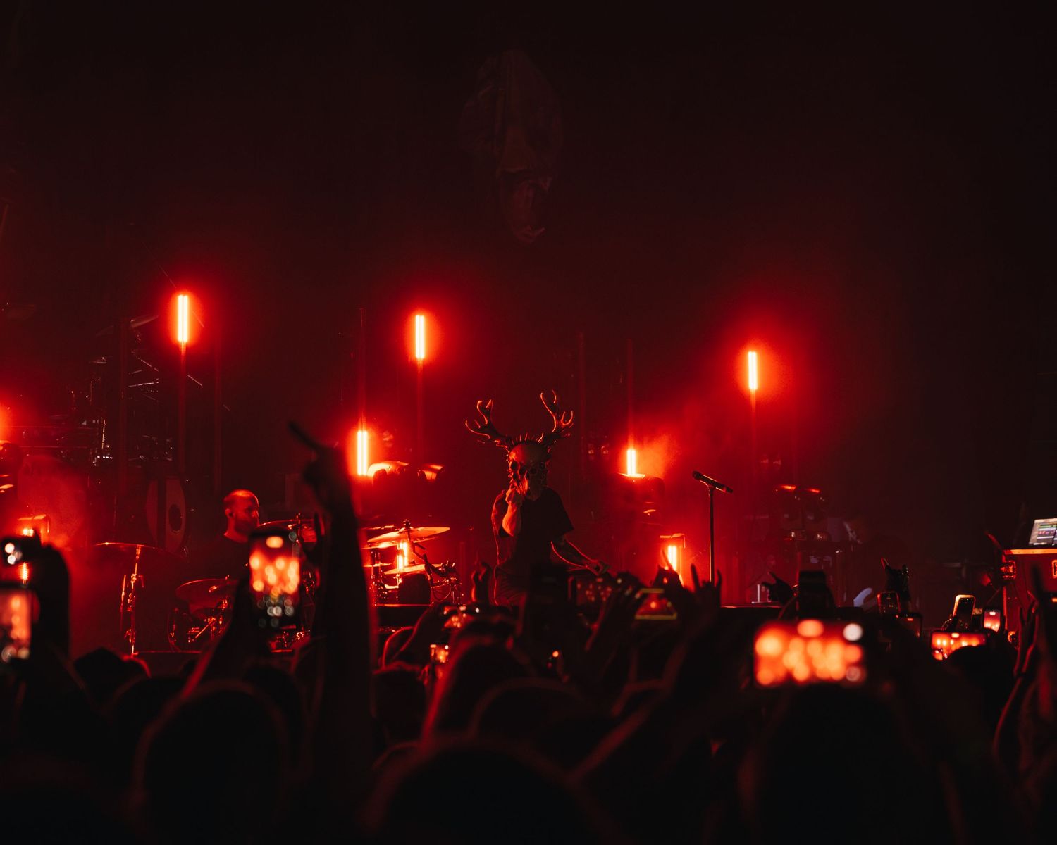 Crowd at a heavy metal concert bathed in dramatic red stage lighting with phones raised.