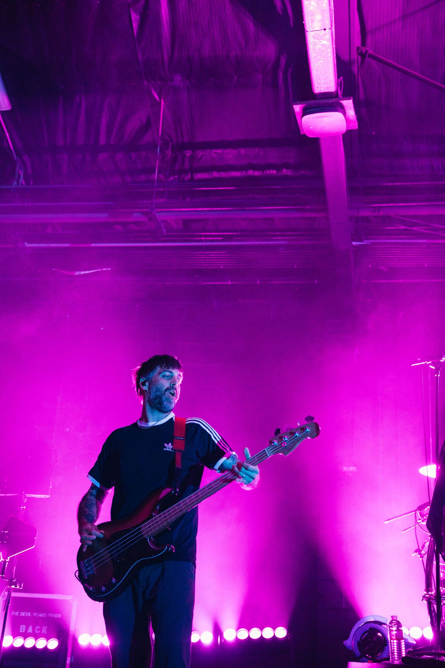 Guitarist performing on stage under vibrant pink and purple lights at a live concert venue.