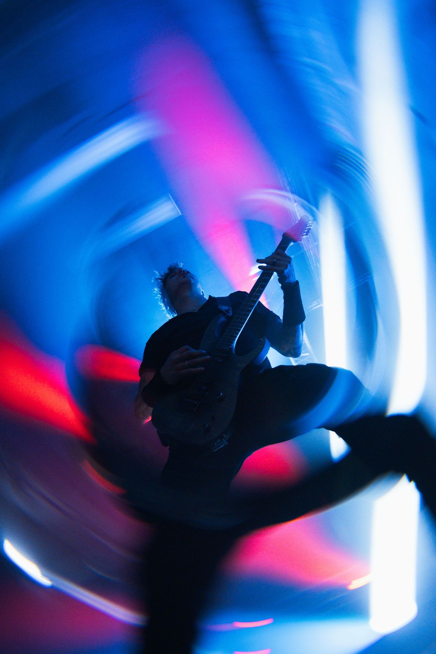 Silhouetted guitarist performs against swirling blue and pink light trails creating a dynamic concert atmosphere.