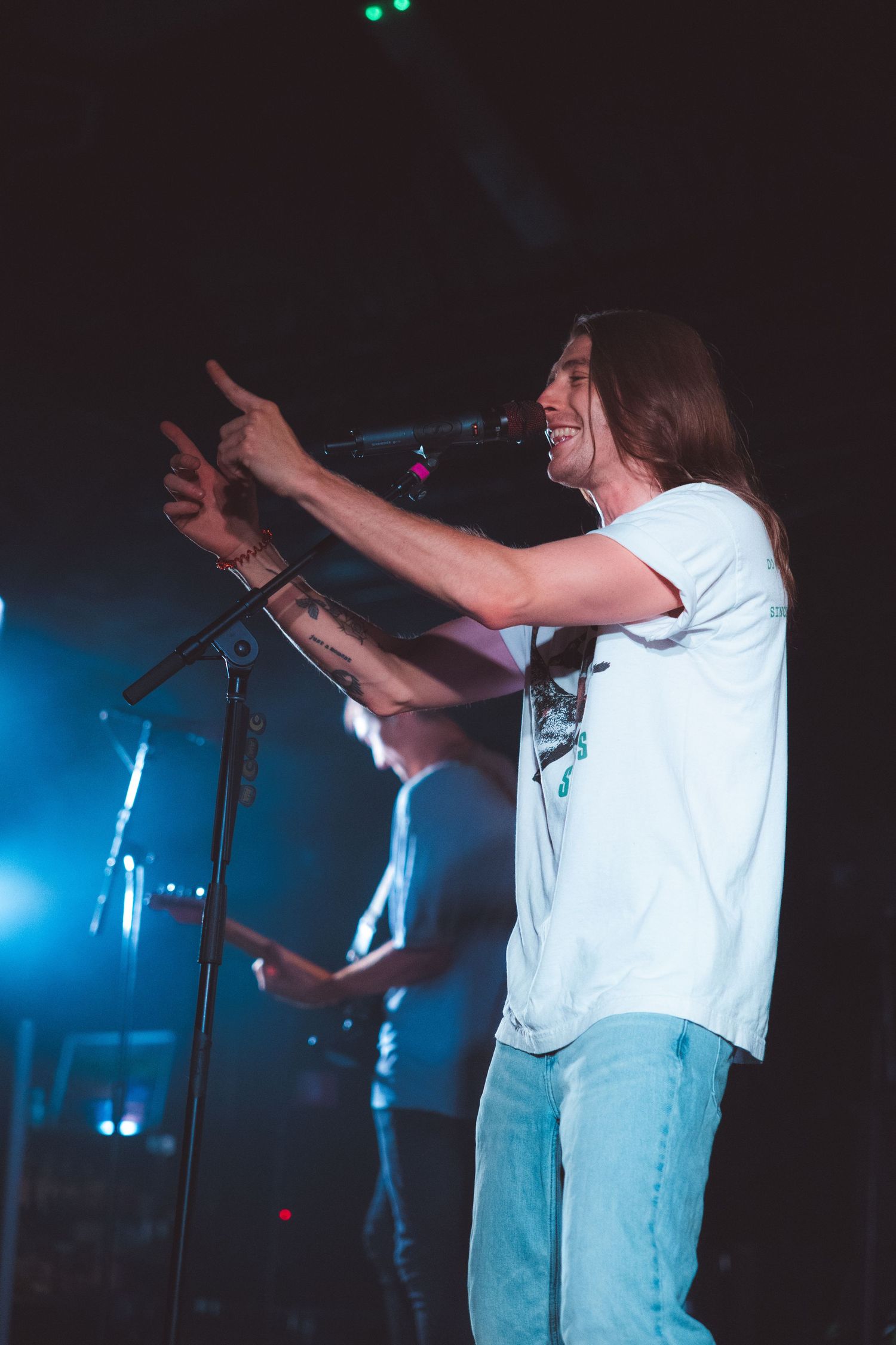Performer in white shirt energetically singing on stage with dramatic blue lighting and dark background.
