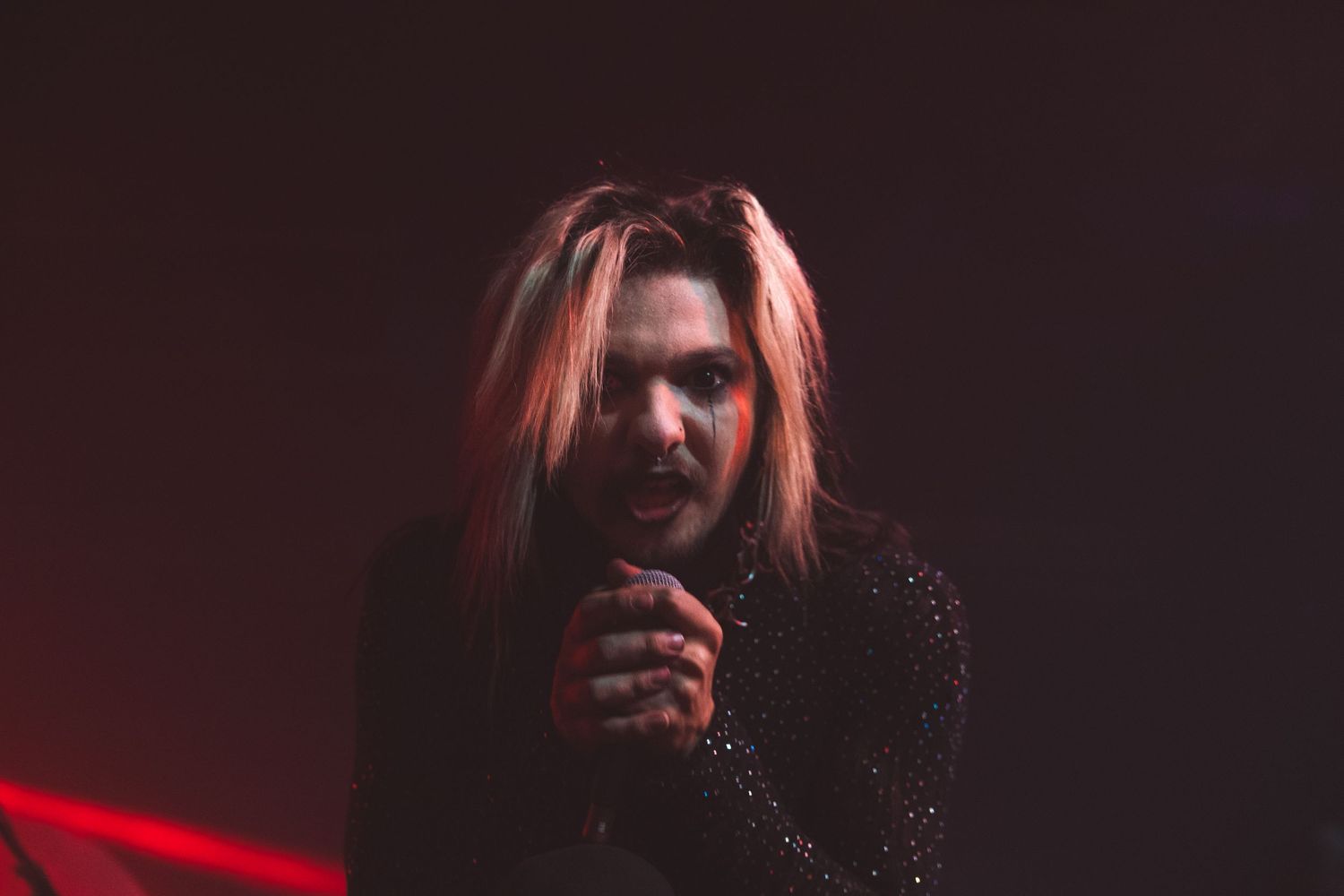 Live music performer illuminated in dramatic red stage lighting during an energetic concert performance.