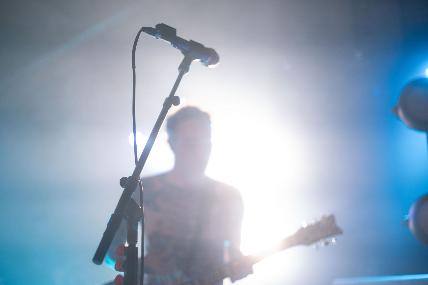 Silhouetted musician performing on stage with microphone against bright backlighting.