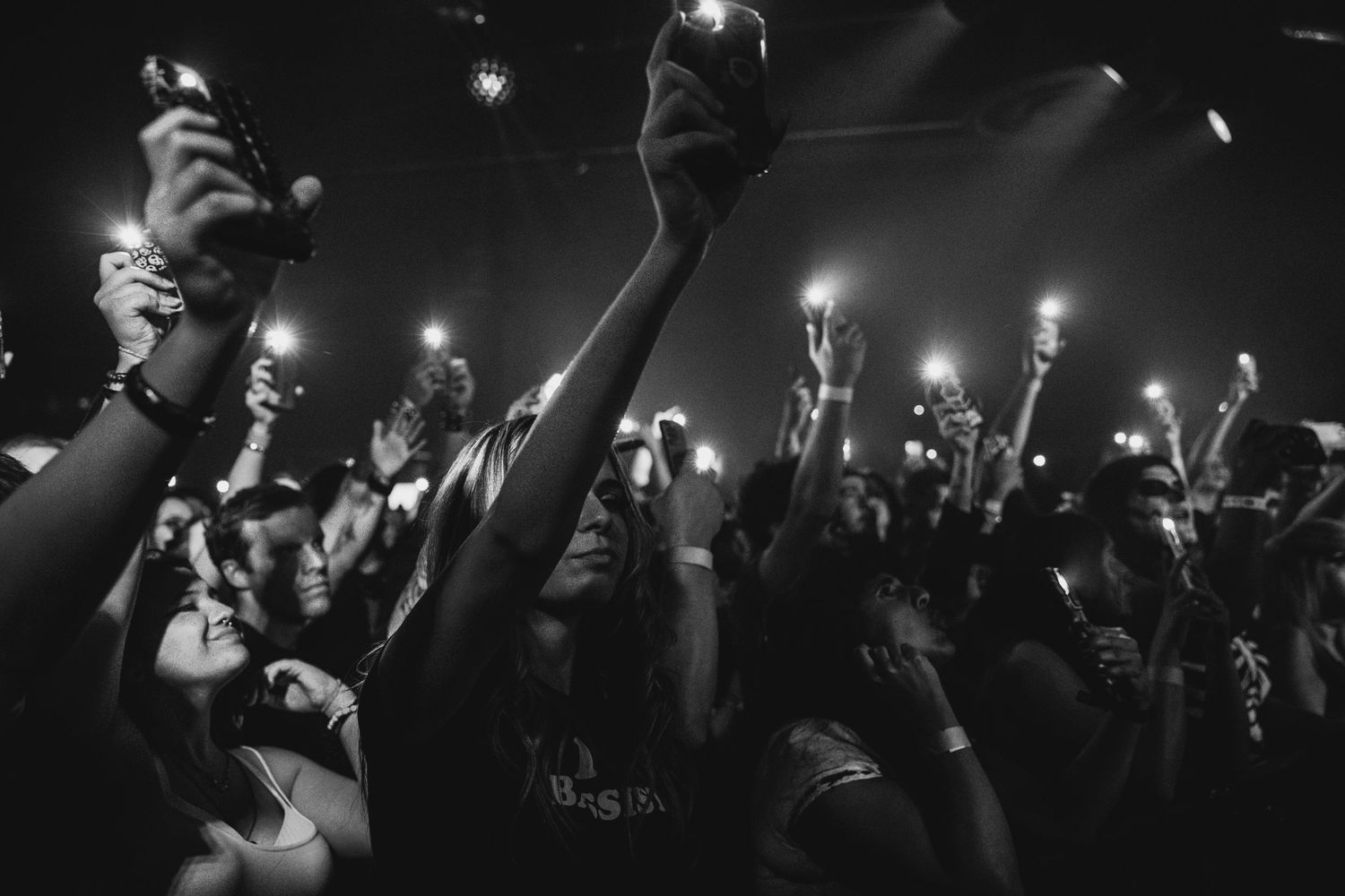 Silhouettes of a crowd raise lights and phones during a dark concert or event.