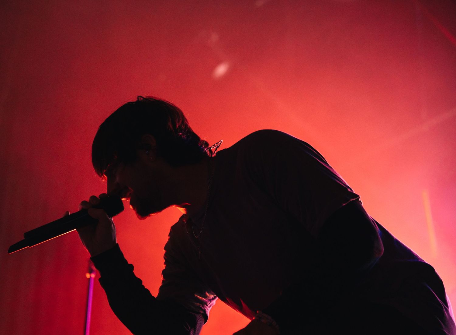A dark silhouetted figure stands on stage in dramatic red lighting during a musical performance.