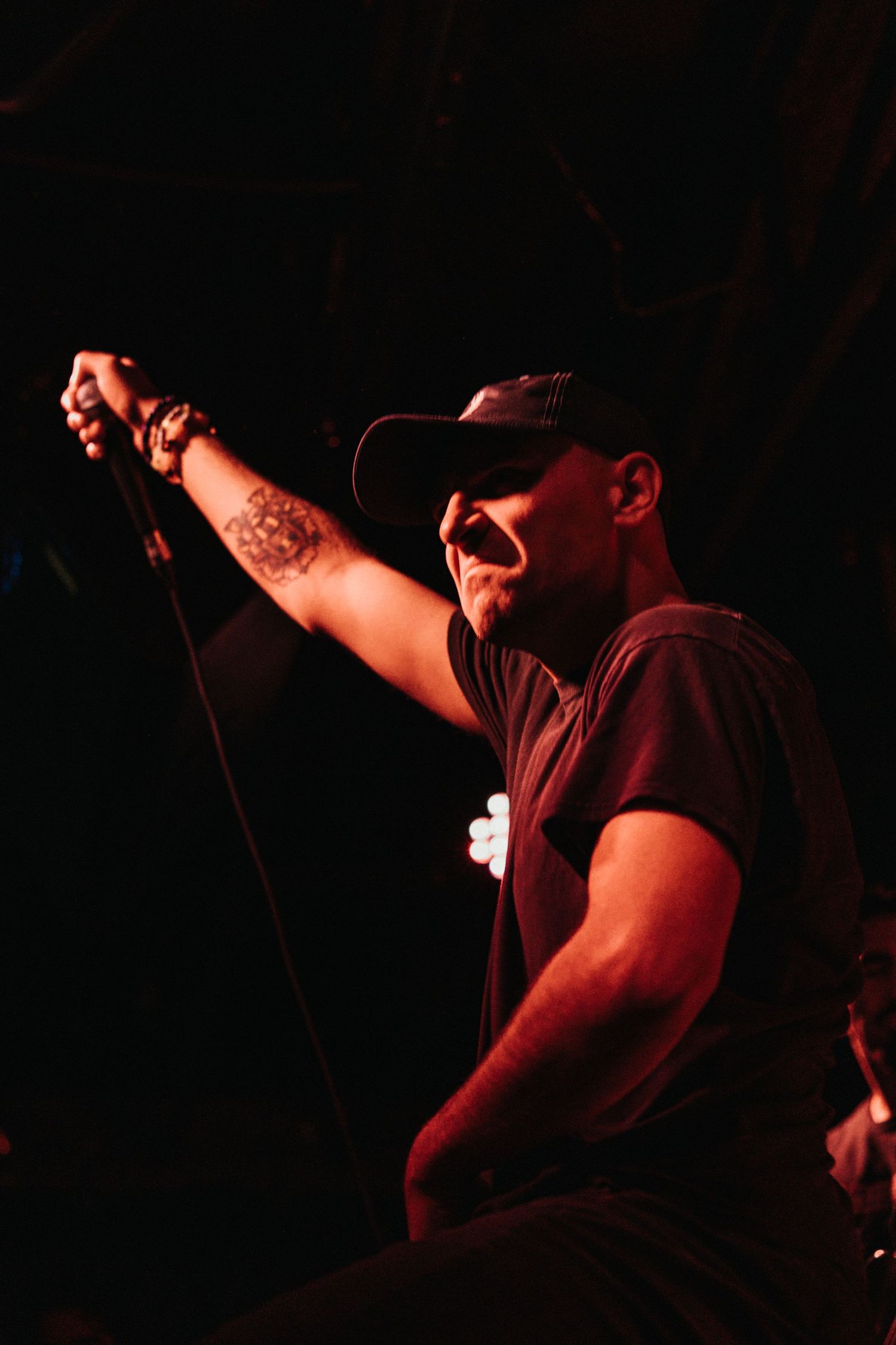 Vocalist passionately performs on dark stage with dramatic red lighting effects.